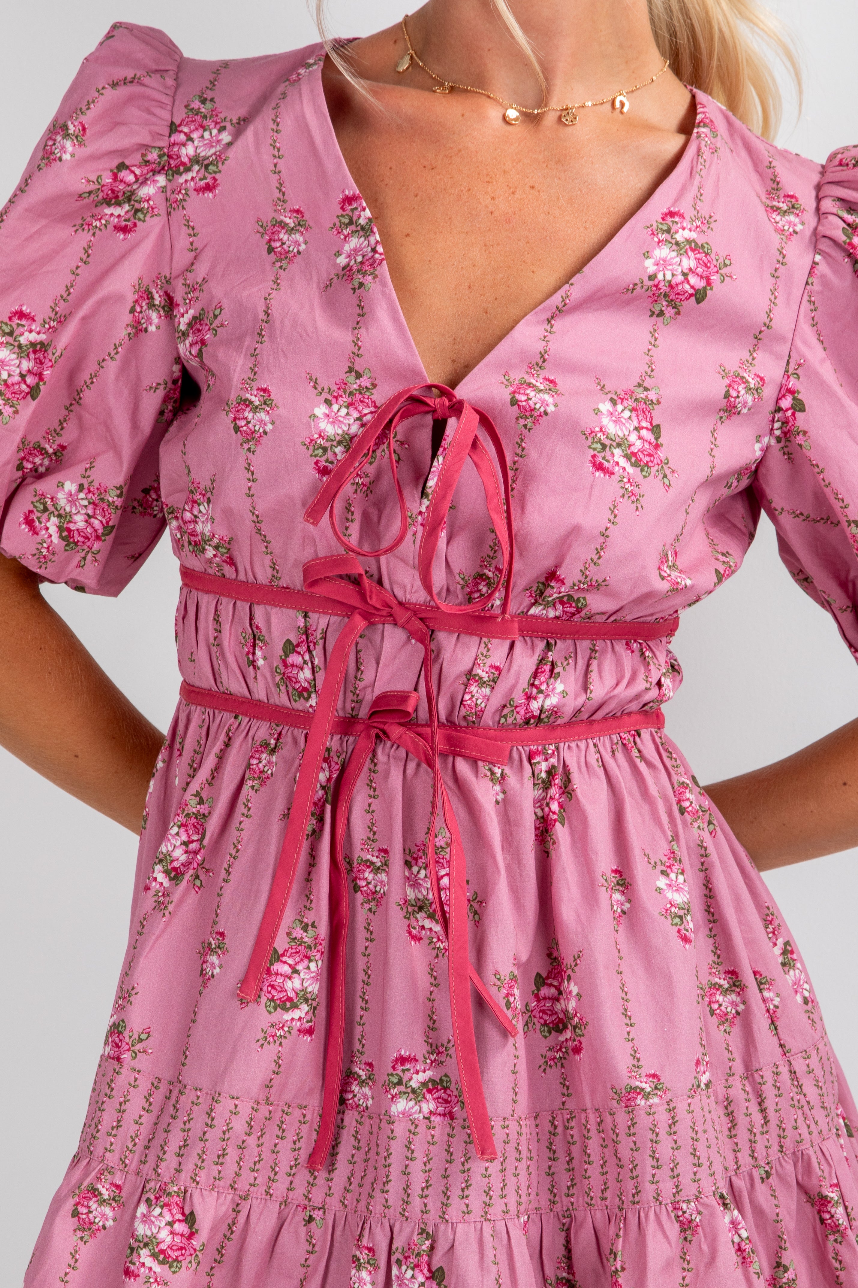 Pink floral dress with a tie waist on a plain background