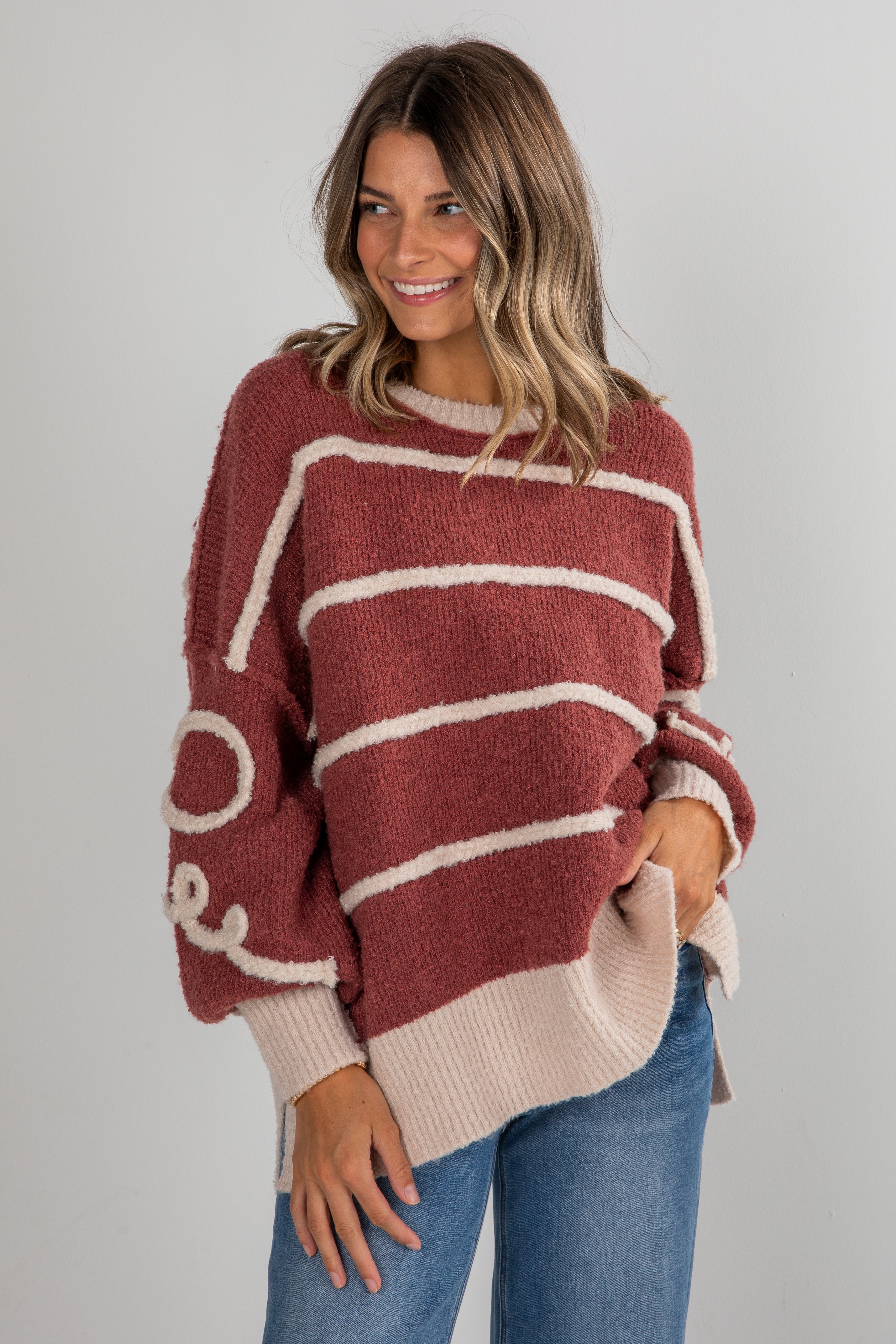 Woman wearing a maroon and beige striped sweater with a plain background