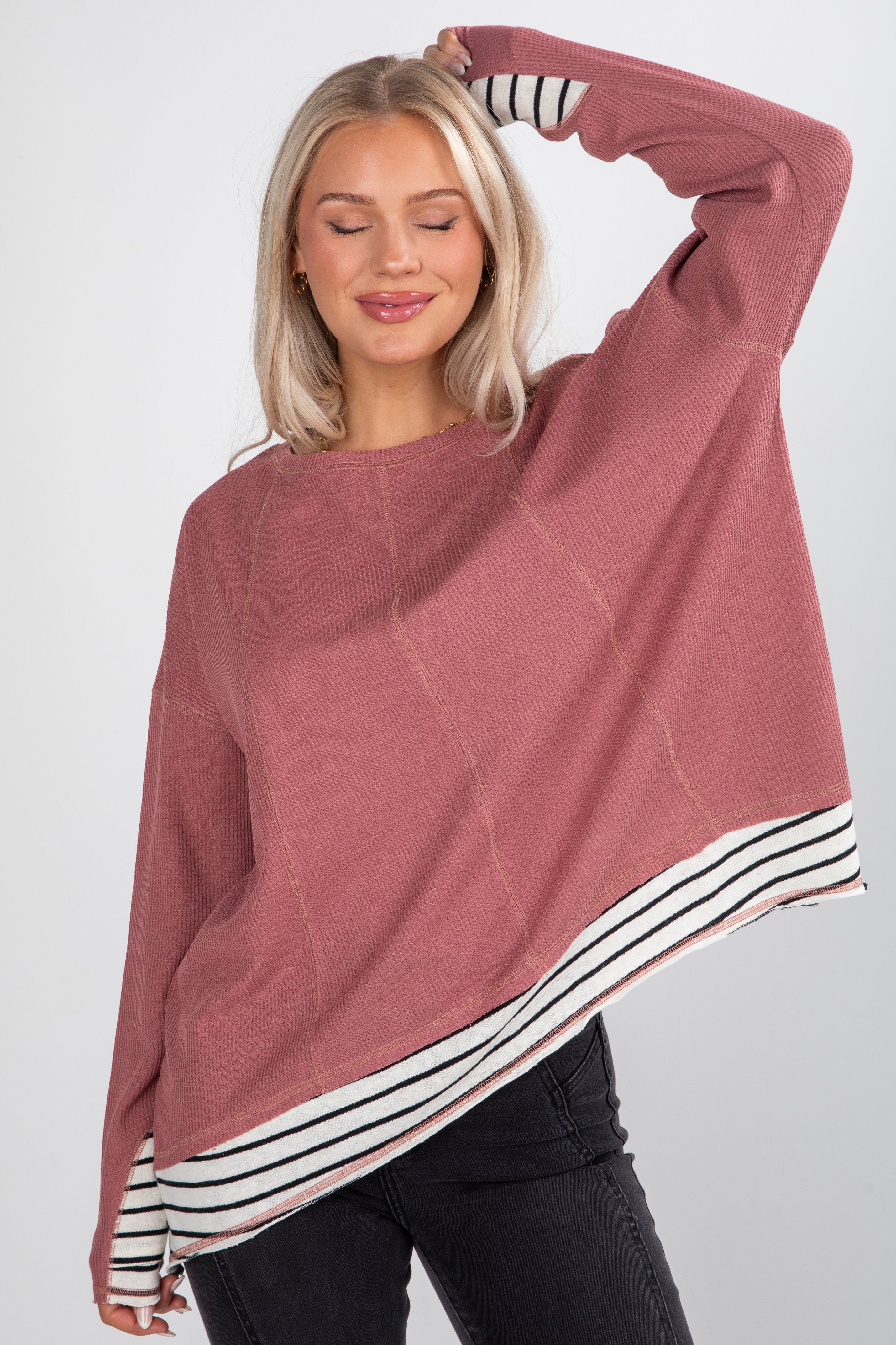 Woman wearing a mauve sweater with a black and white striped hem on a plain background