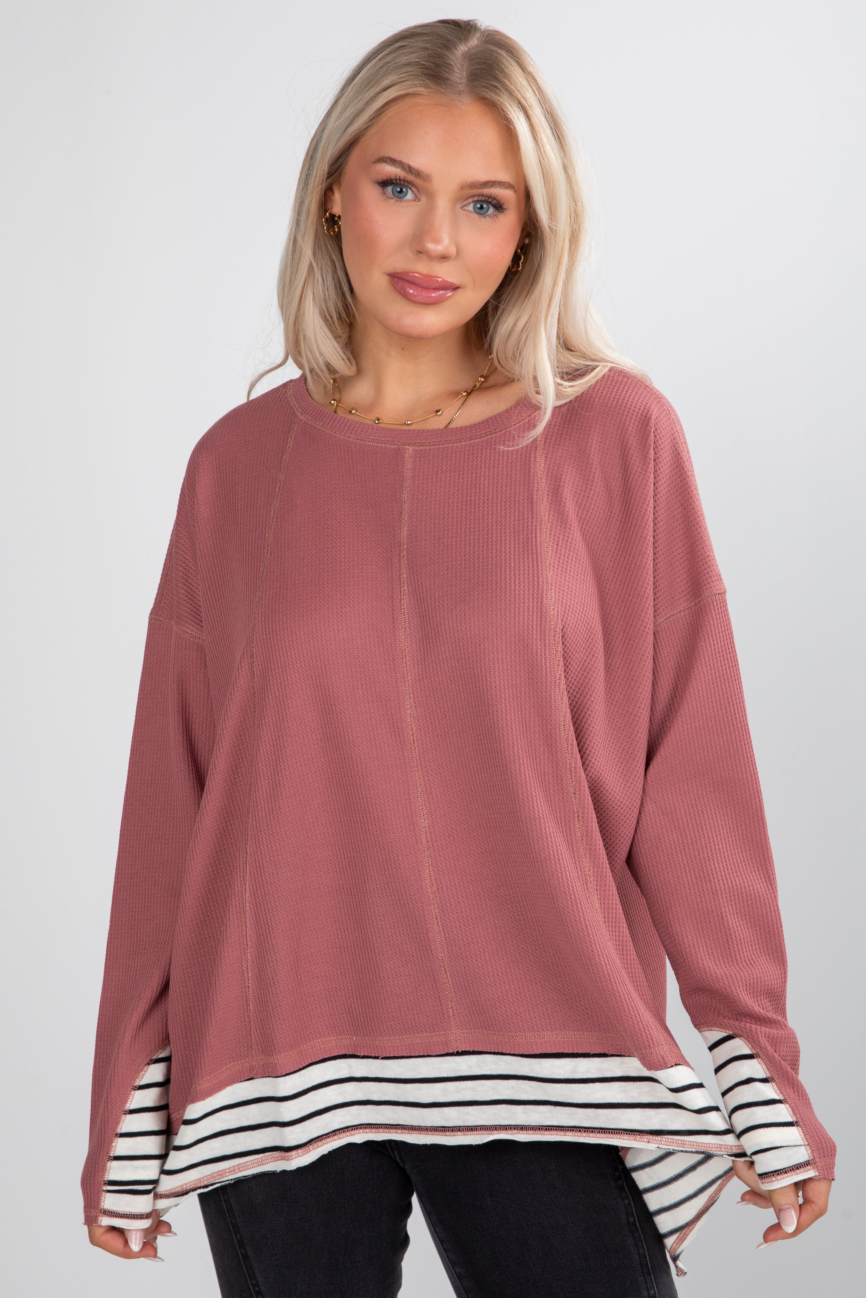 Woman wearing a pink long-sleeve top with a striped hem on a white background