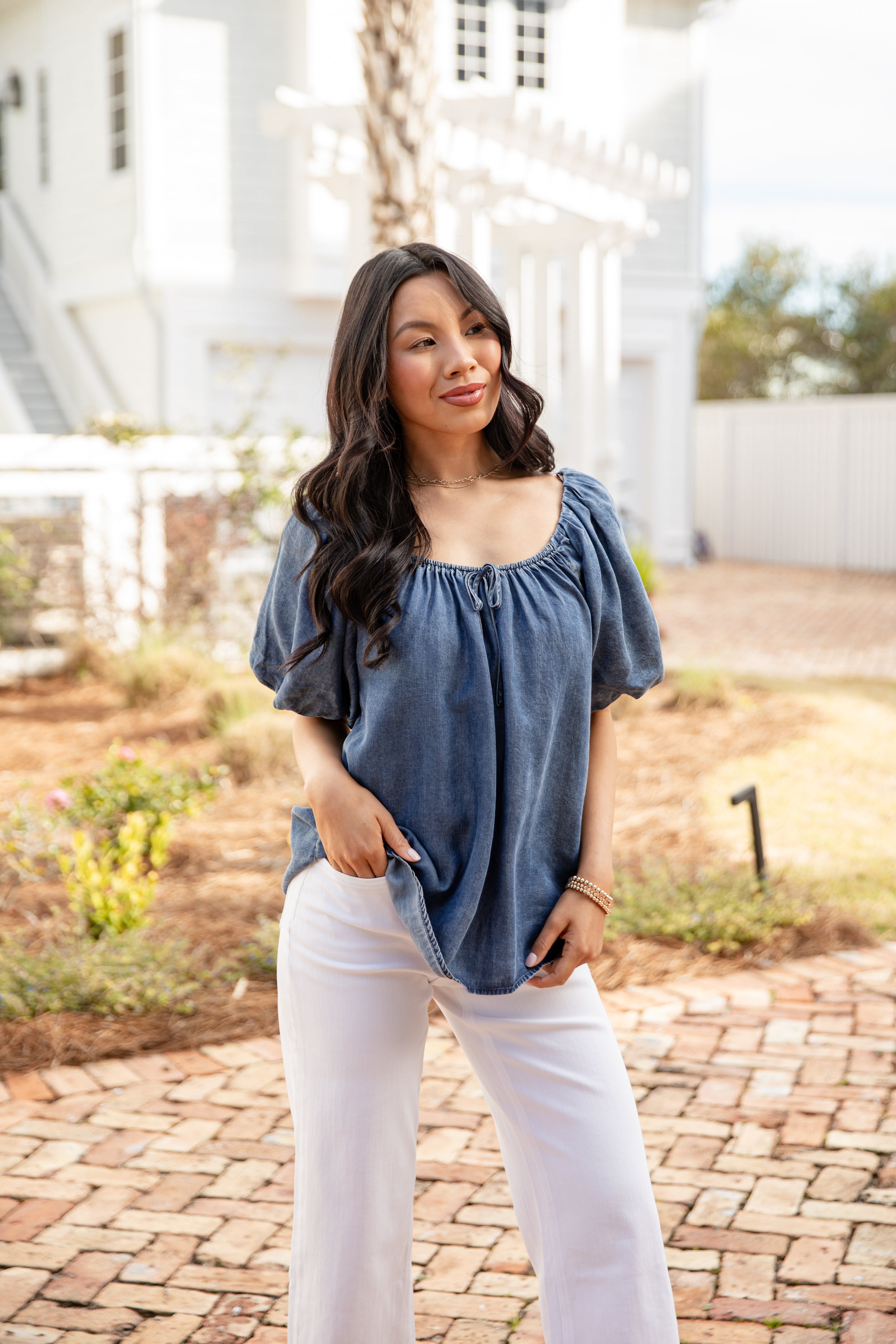 Woman wearing a blue top and white pants standing outdoors.