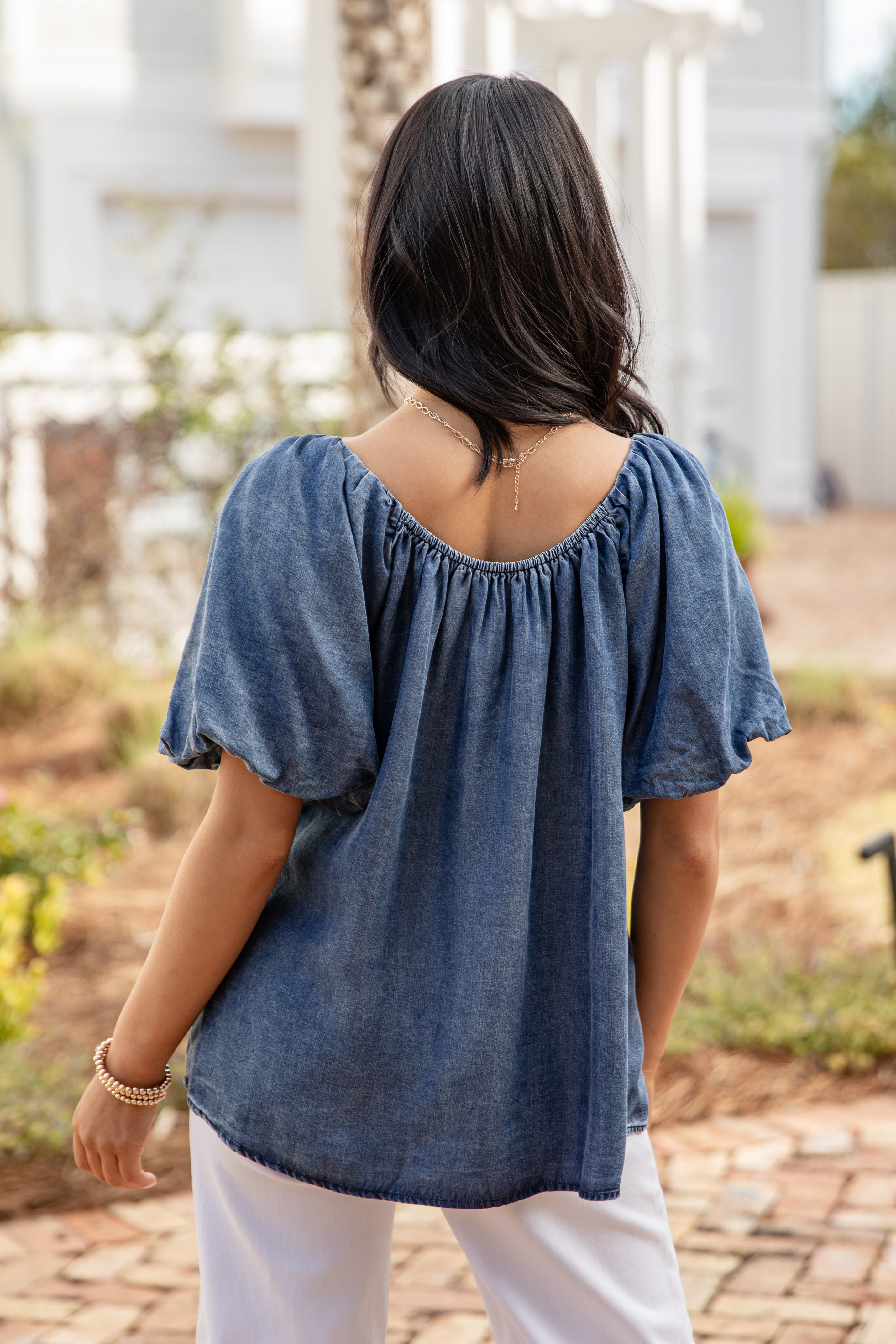 Woman wearing a blue top and white pants standing outdoors.