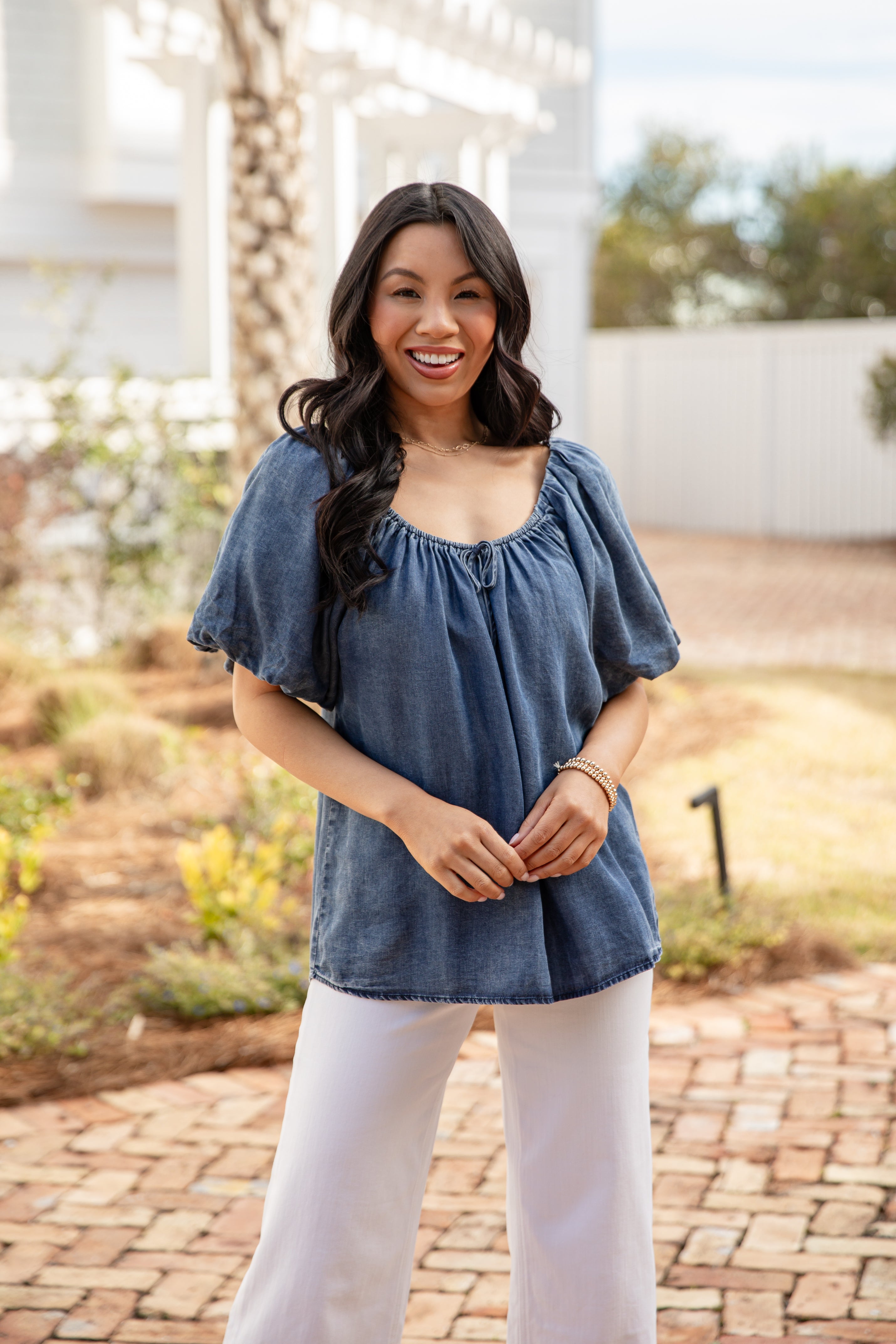 Woman wearing a blue top and white pants standing outdoors.