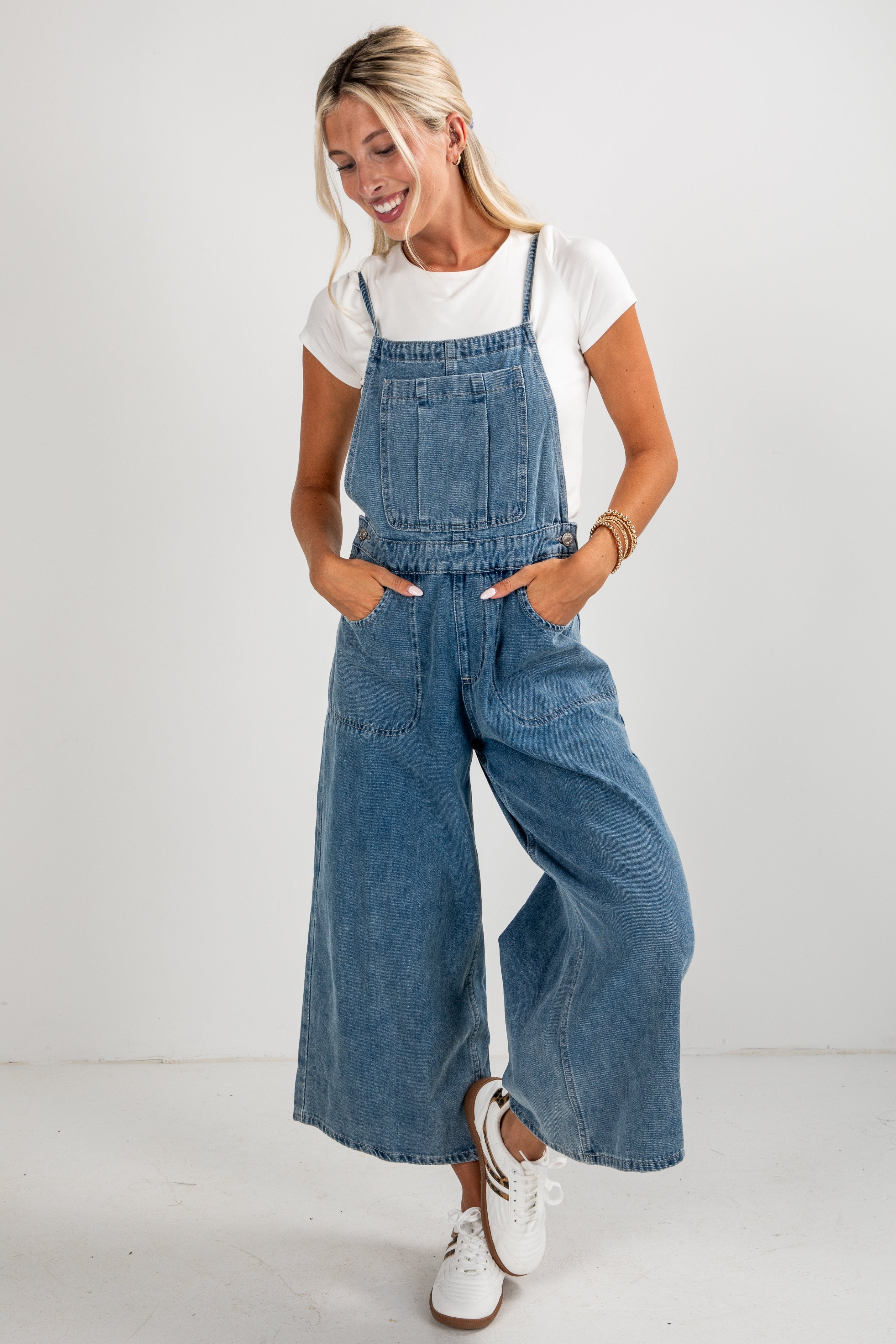 Woman wearing blue denim overalls and white sneakers on a plain background