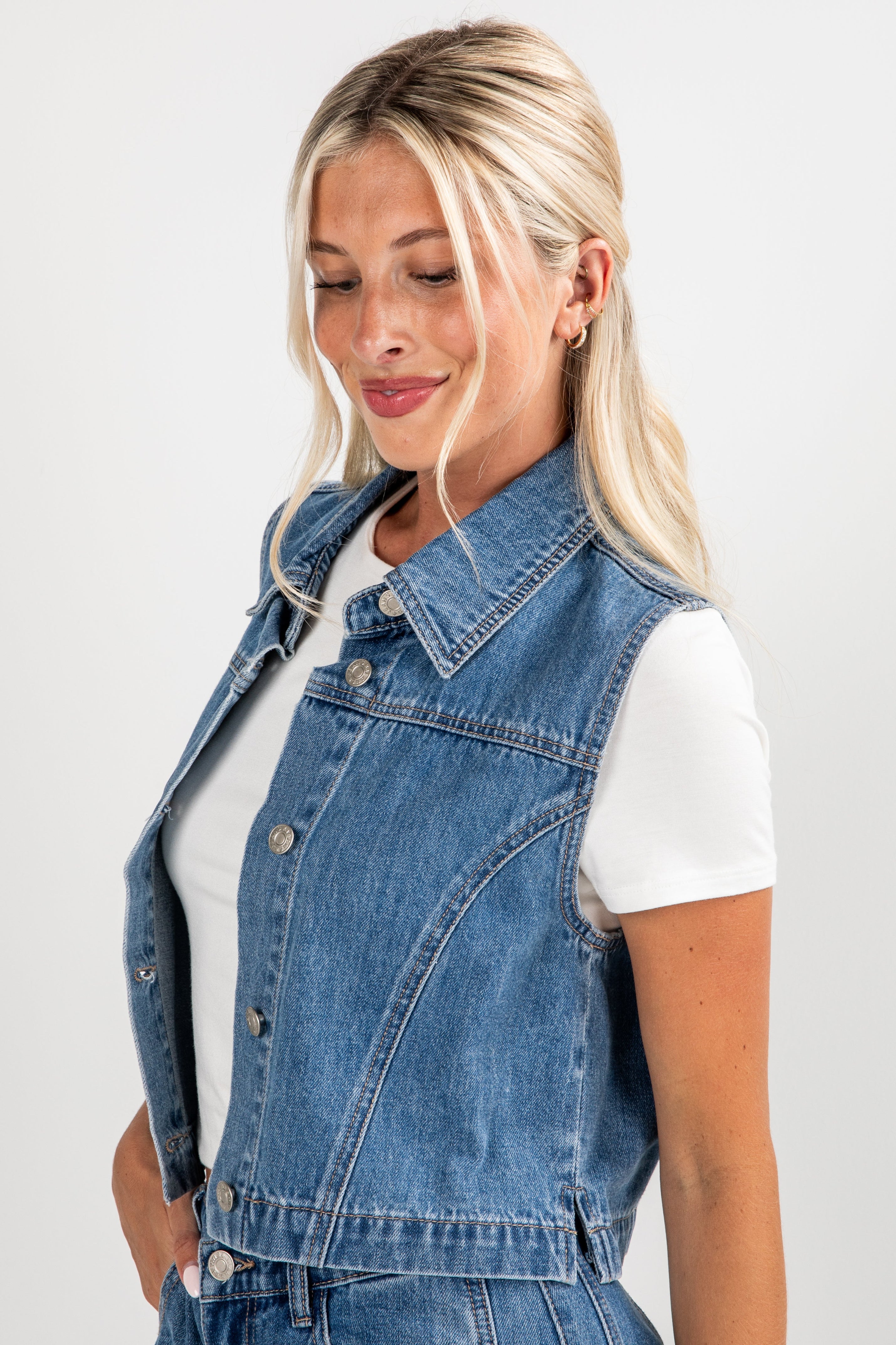 Woman wearing a denim vest over a white shirt on a plain background