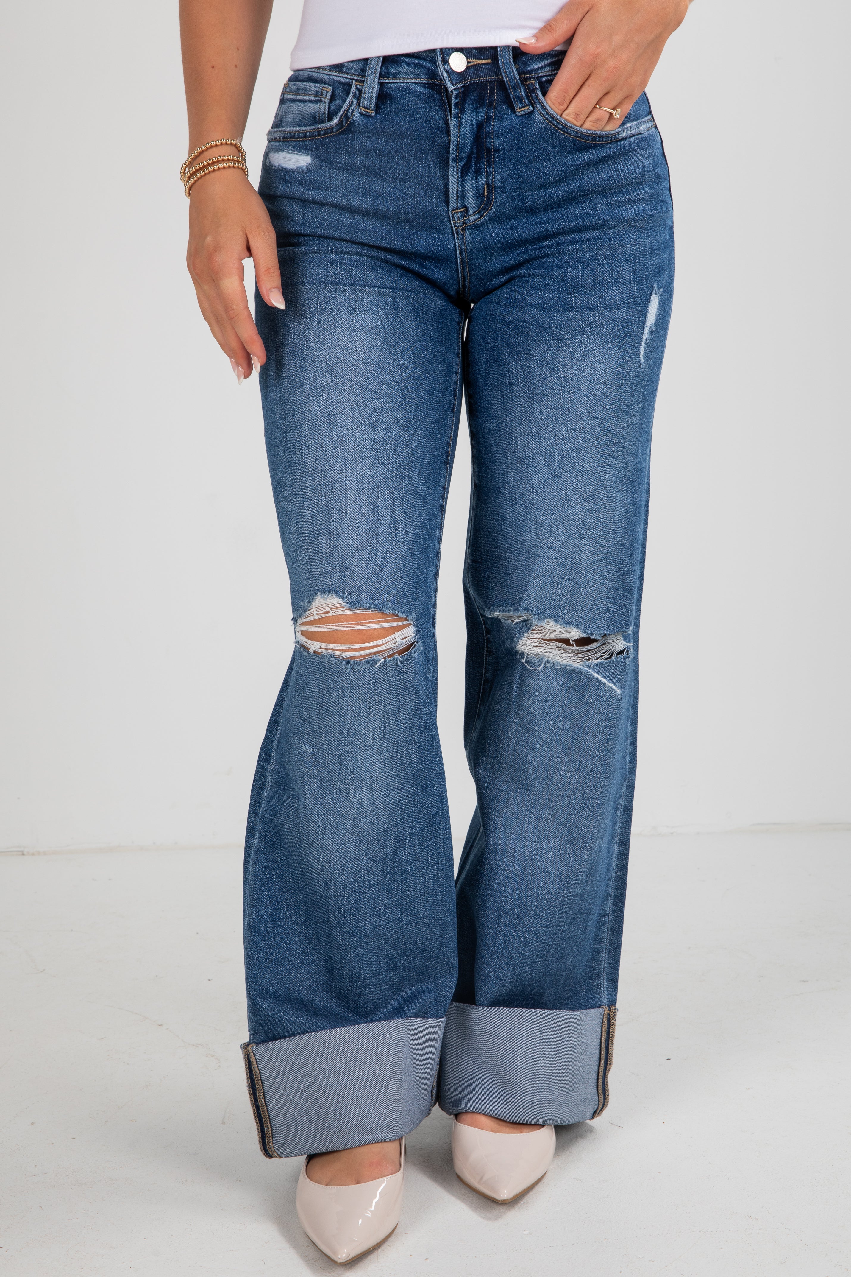 Person wearing blue jeans with distressed details on a white background