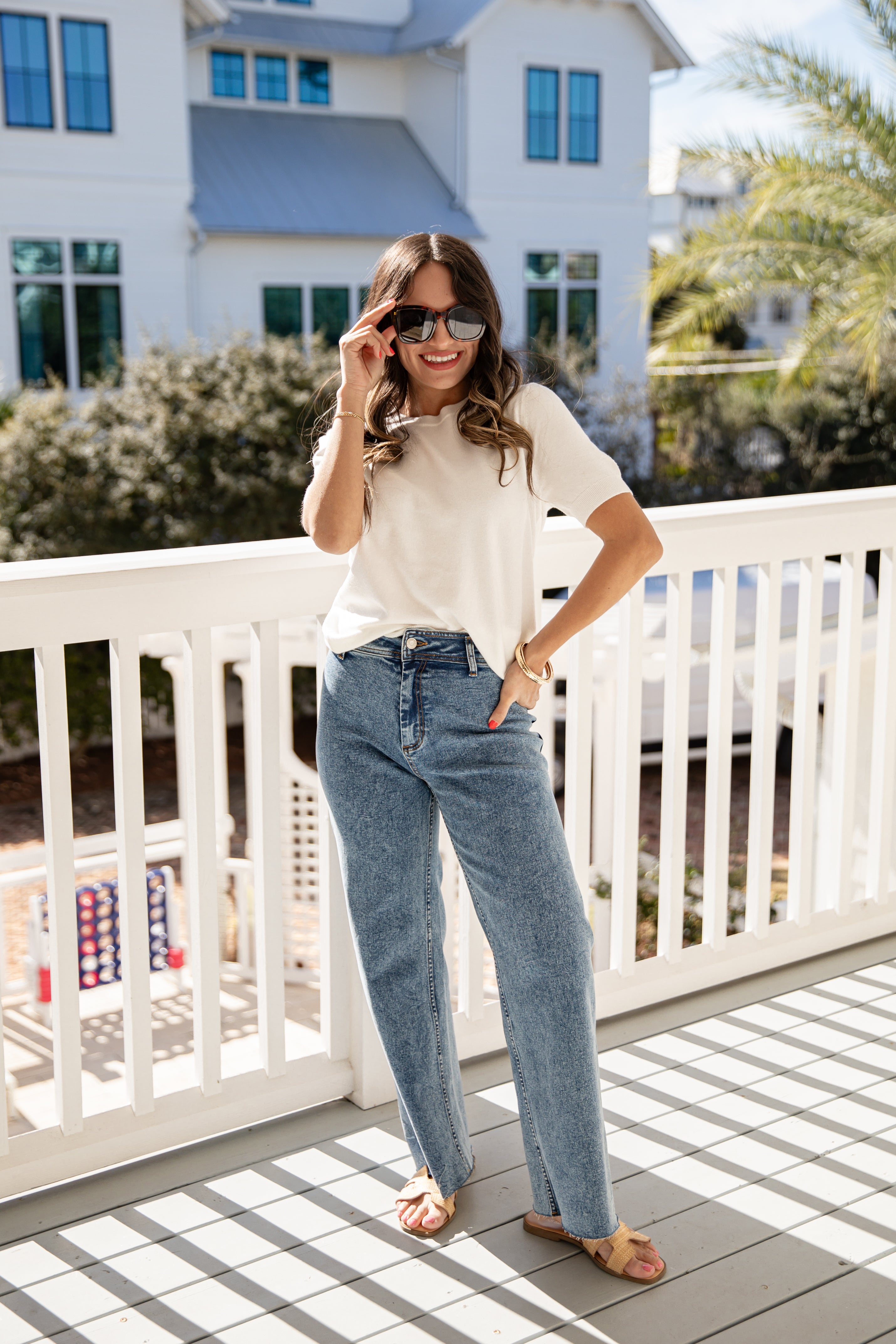Woman standing on a balcony wearing sunglasses and casual clothing.