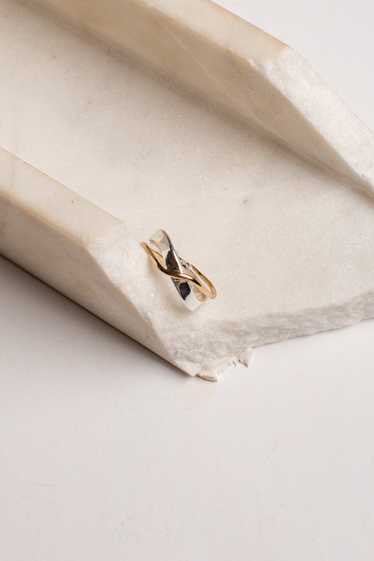 A delicate gold and silver twisted ring resting on a textured, off-white stone surface.