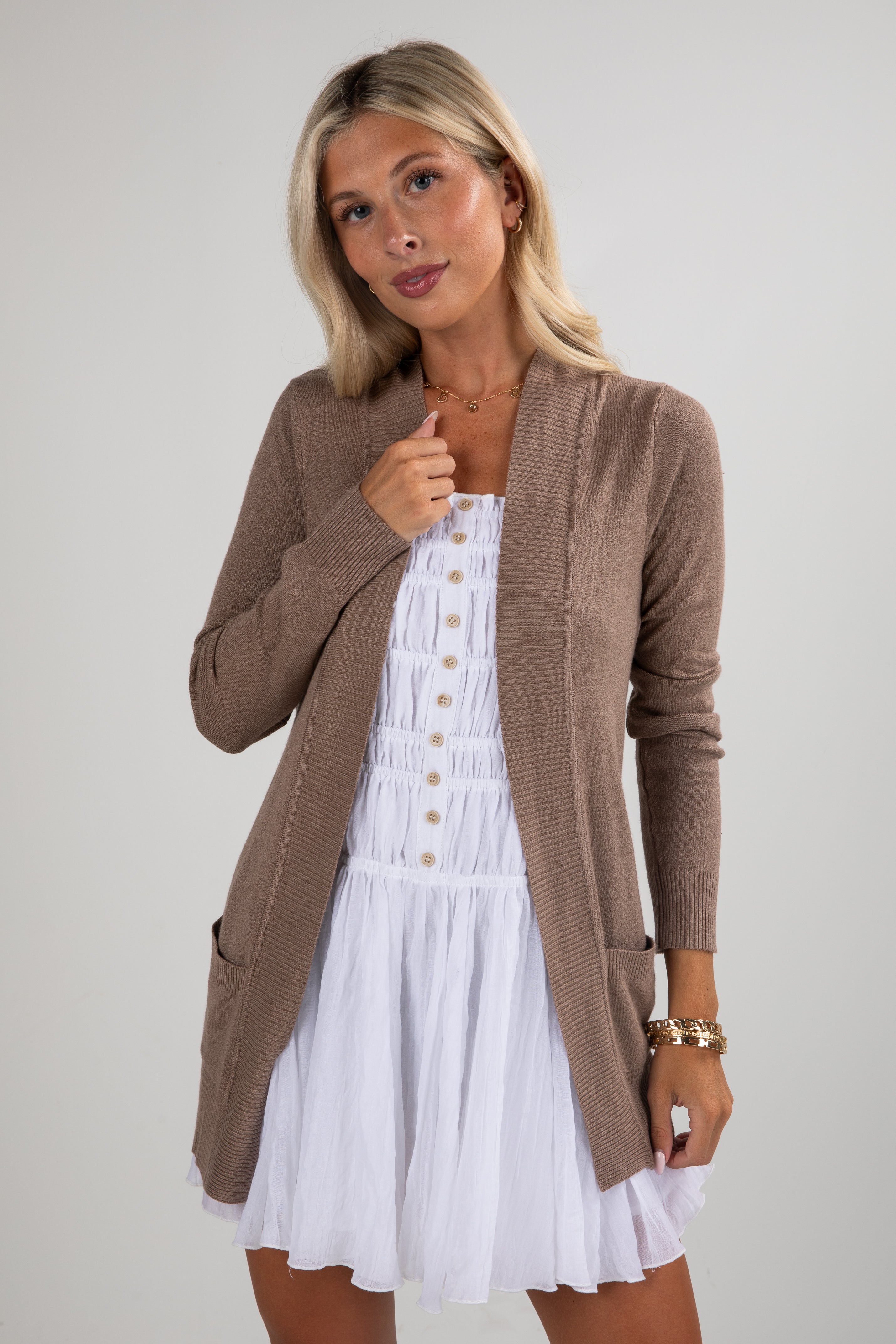 Woman wearing a brown cardigan over a white dress on a plain background