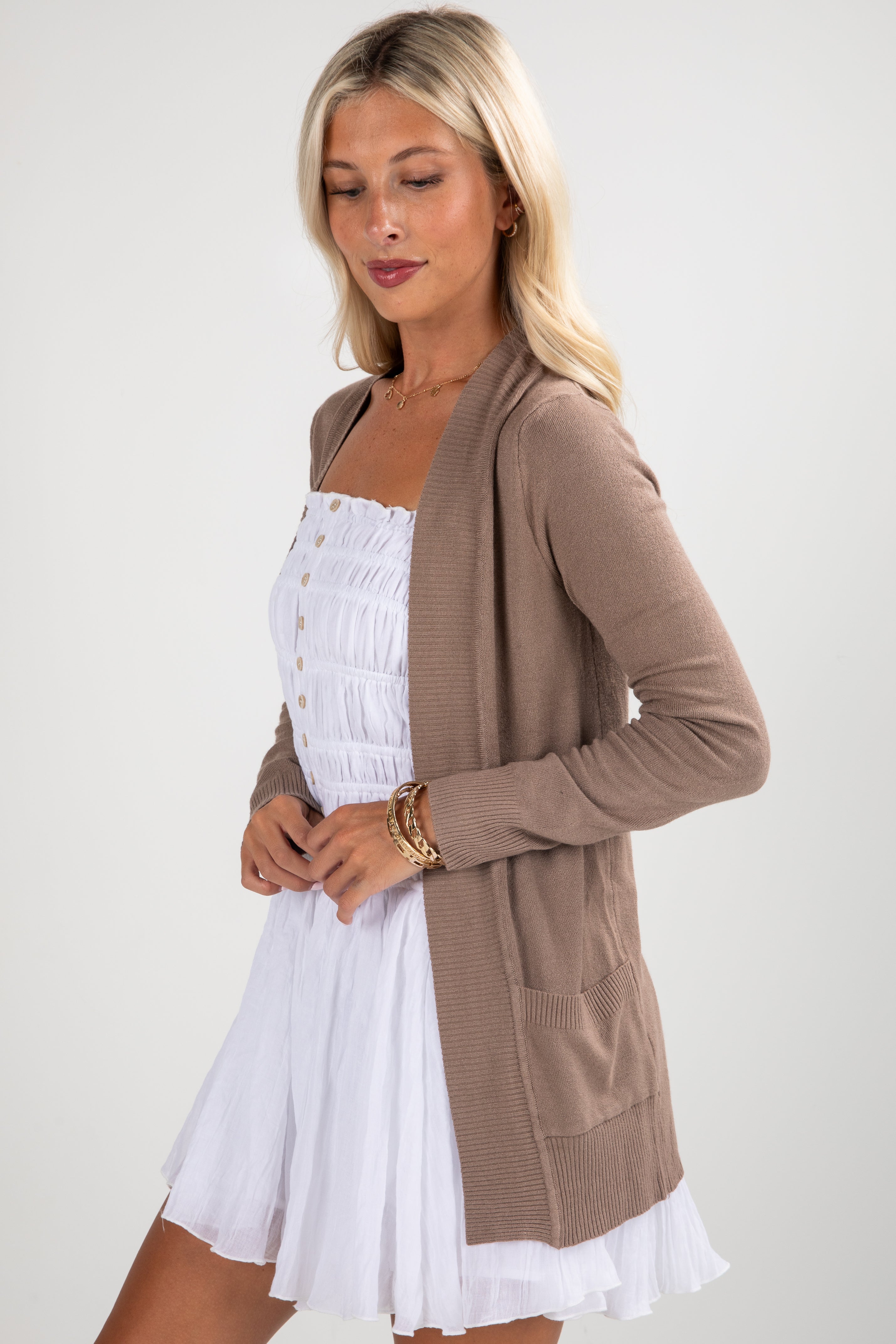 Woman wearing a brown cardigan over a white dress on a plain background