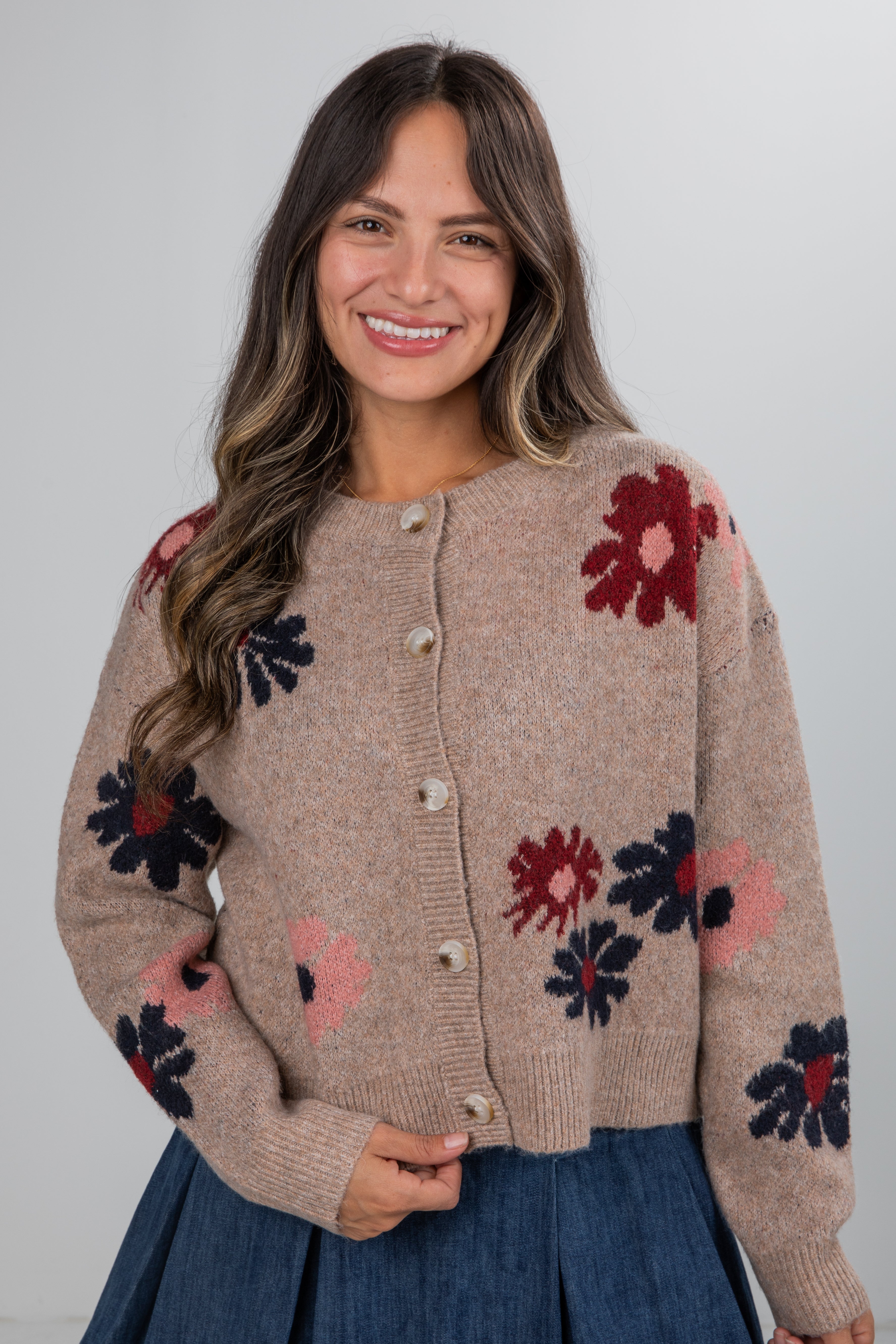Woman wearing a beige cardigan with floral patterns on a plain background