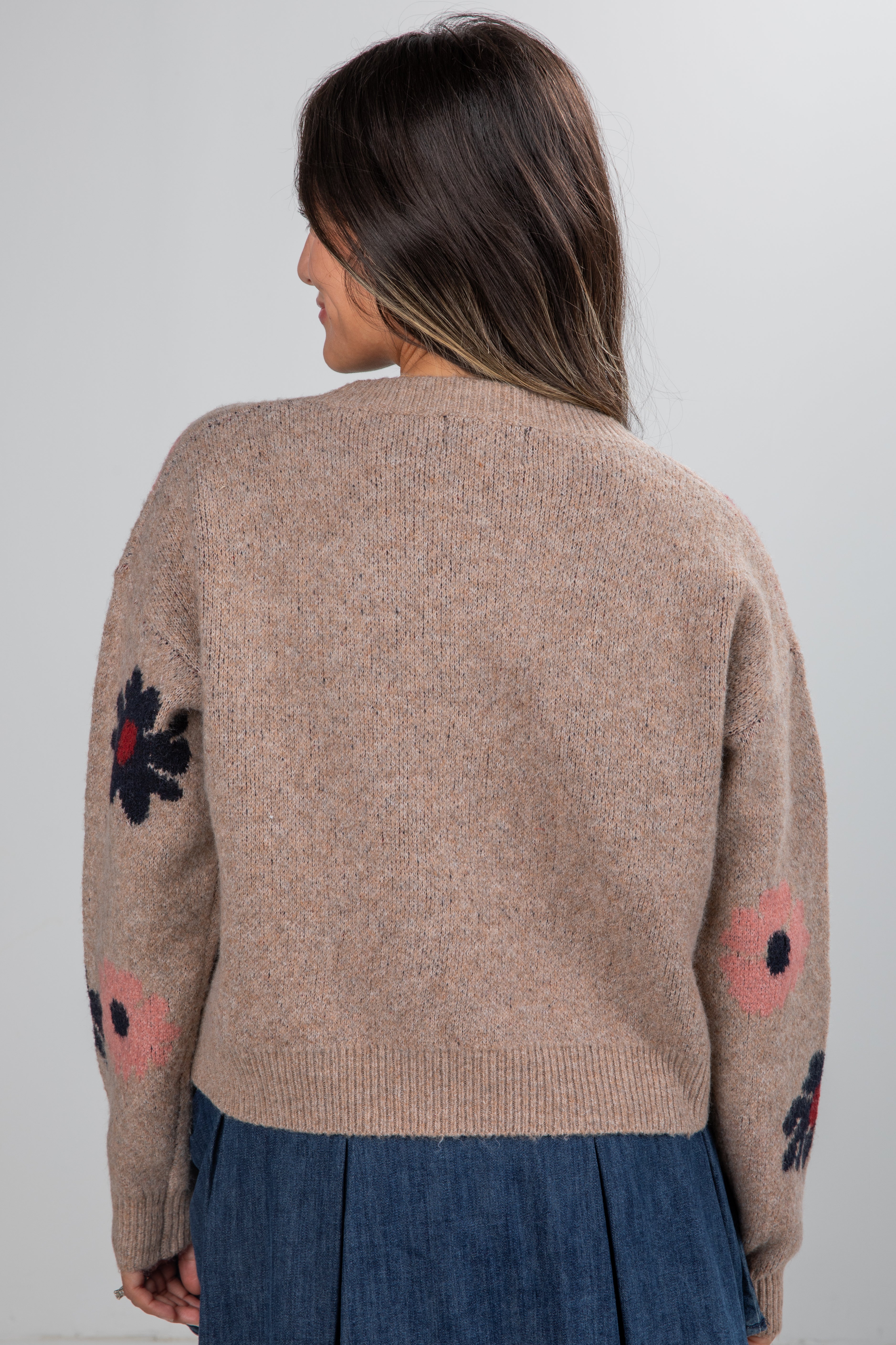 Beige sweater with colorful flower patterns worn by a person on a plain background