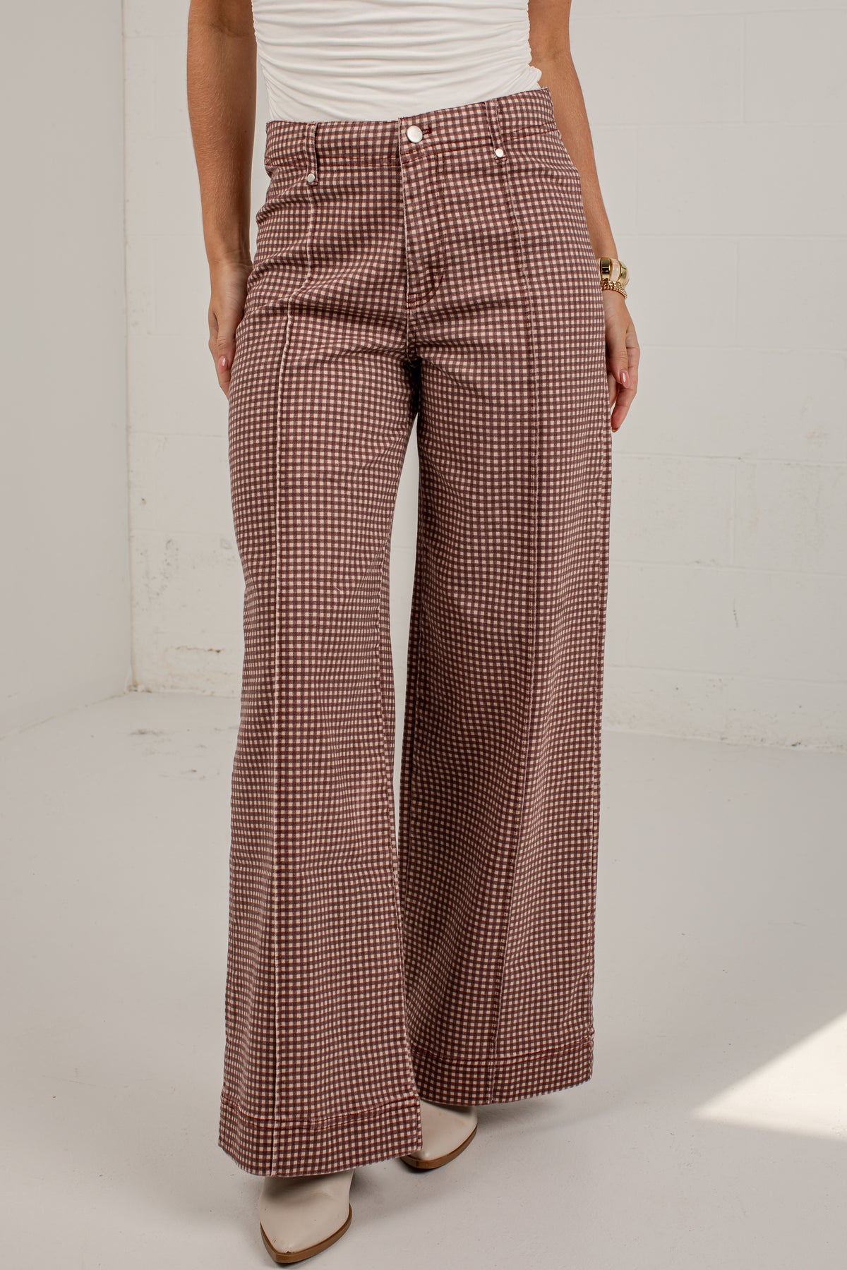 A model wearing high-waisted, wide-leg trousers with a brown and beige houndstooth pattern, paired with a white top and beige boots.