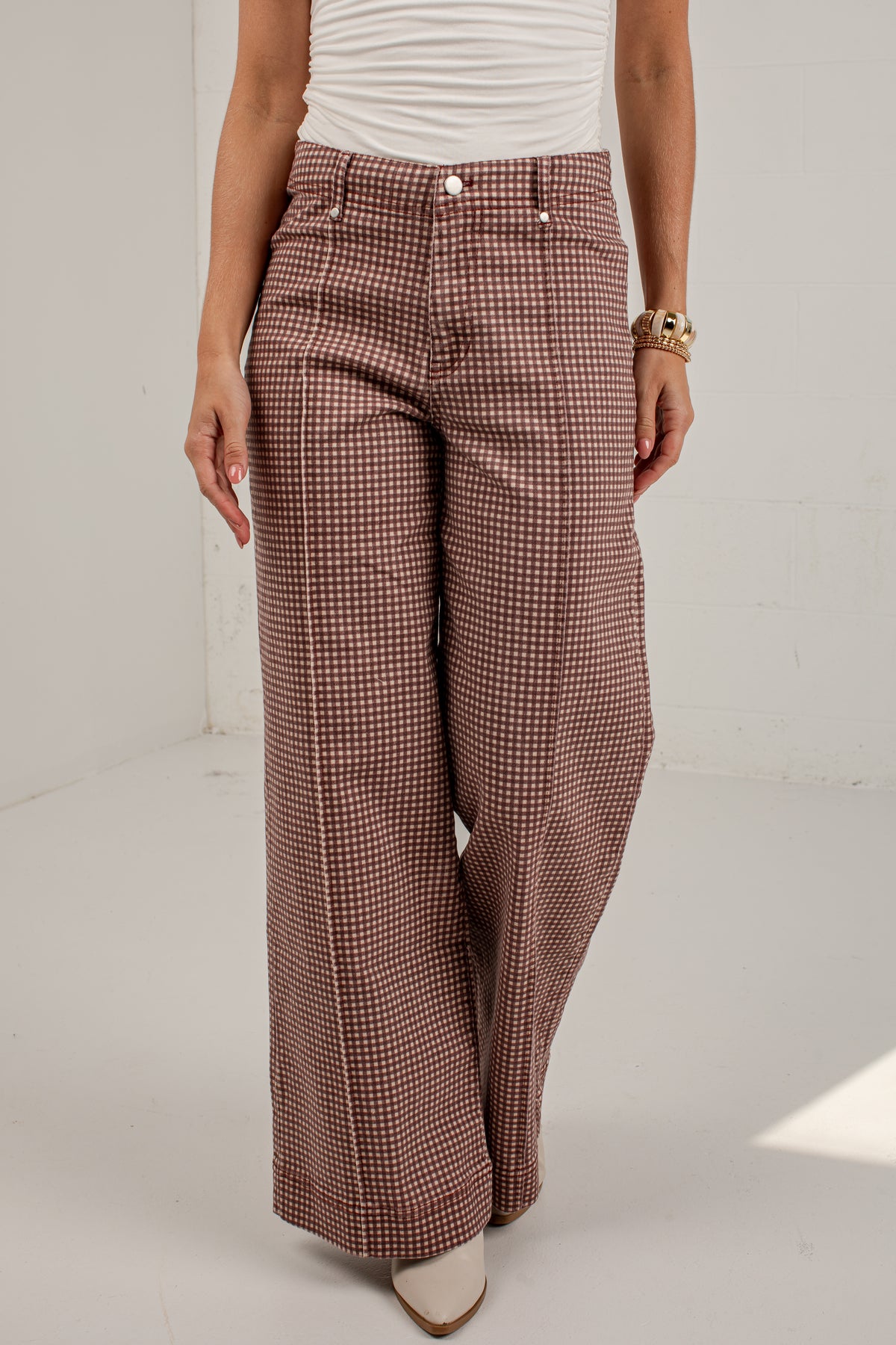 A person wearing high-waisted, wide-leg trousers with a small-scale brown and beige houndstooth pattern, paired with a white ribbed top and beige pointed-toe heels.
