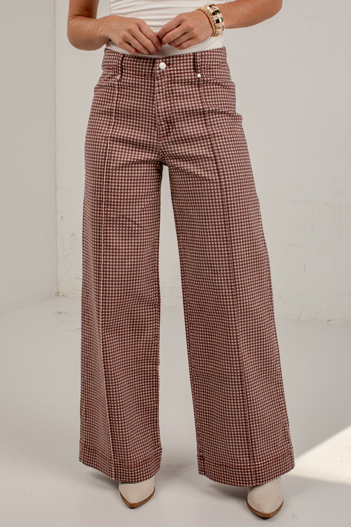 A person wearing high-waisted, wide-leg trousers with a small-scale brown and white houndstooth pattern, paired with a white top and white pointed-toe heels.