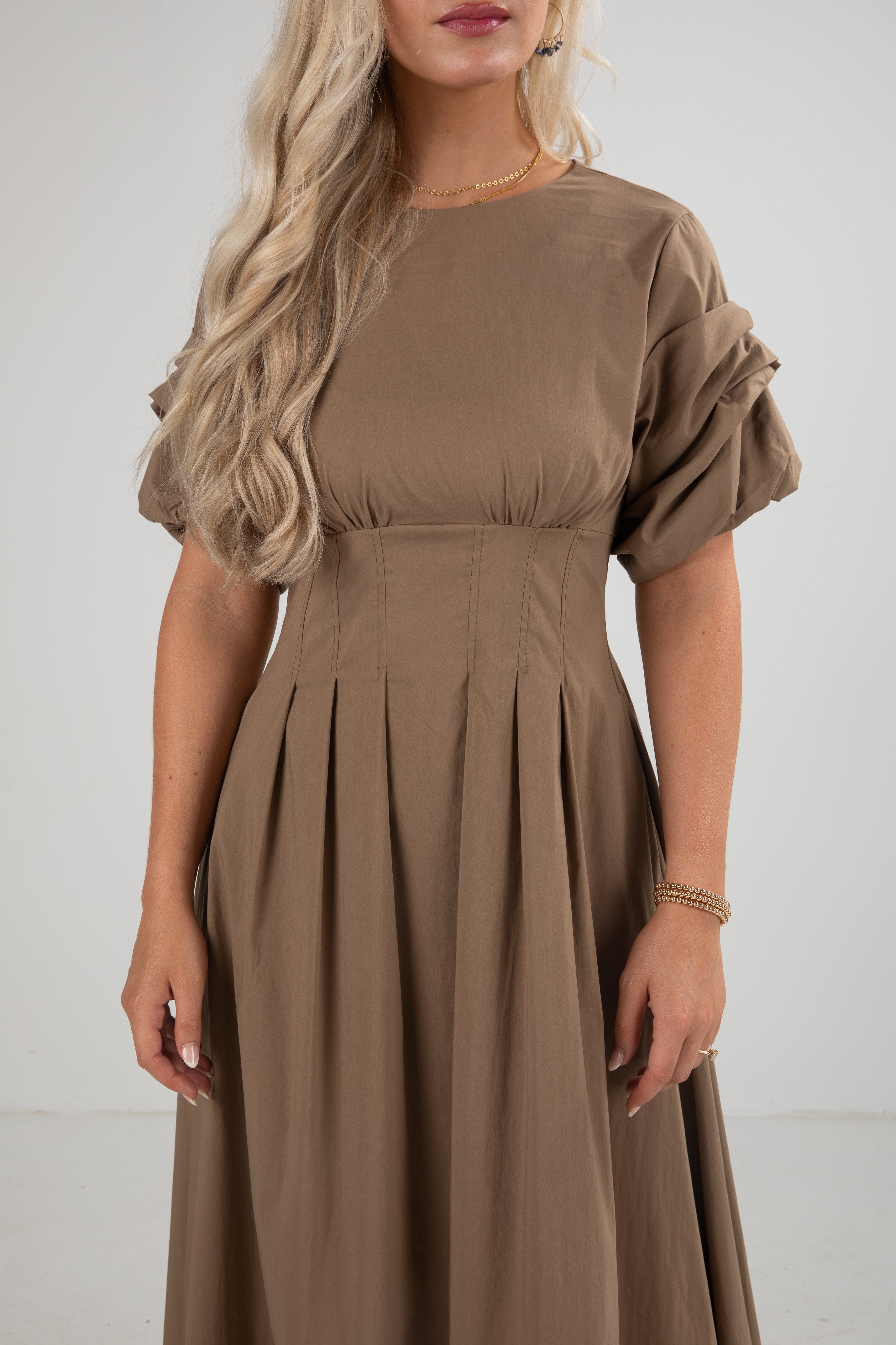 Woman wearing a brown dress with ruffled sleeves against a white background