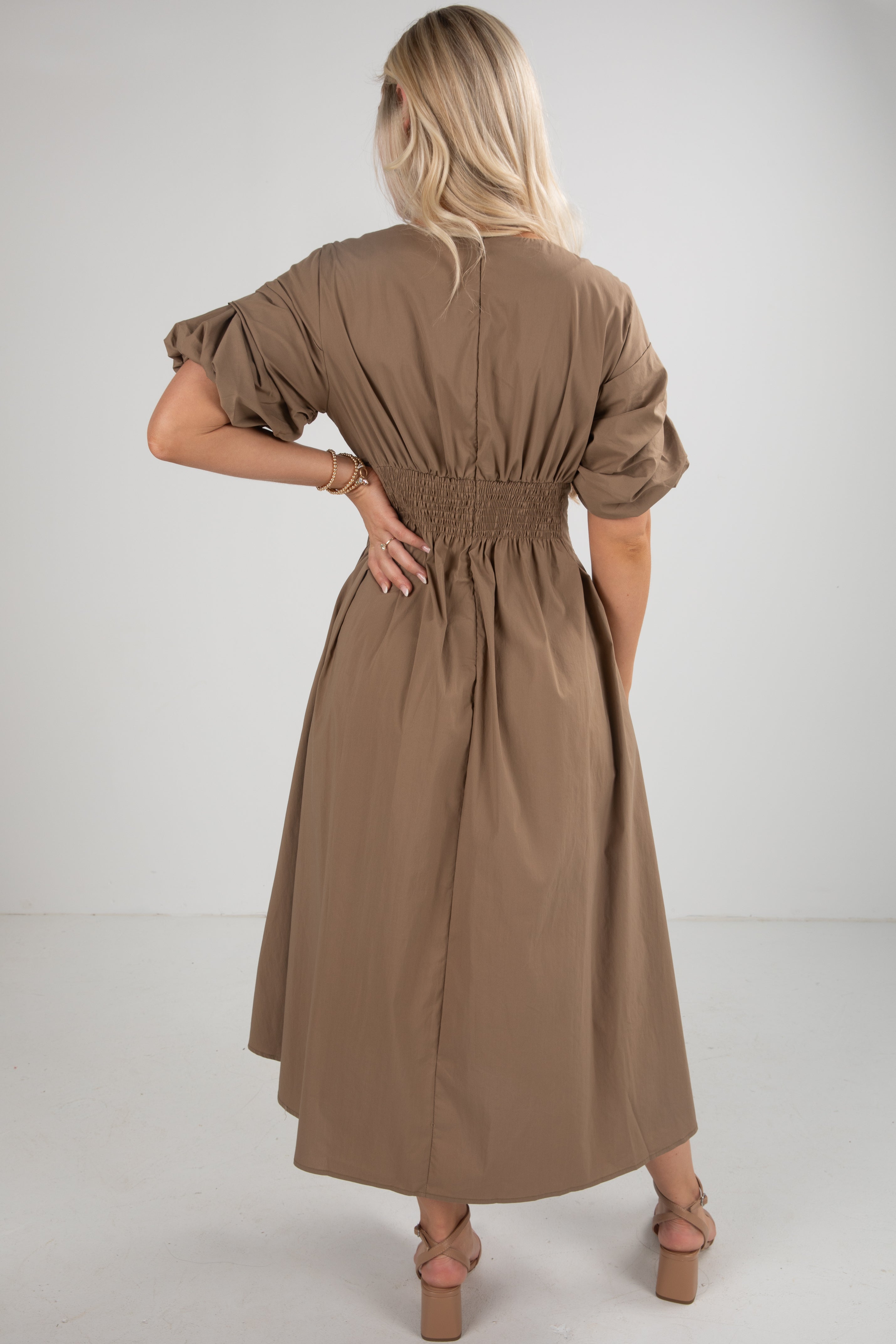 Woman wearing a brown dress with puff sleeves on a white background