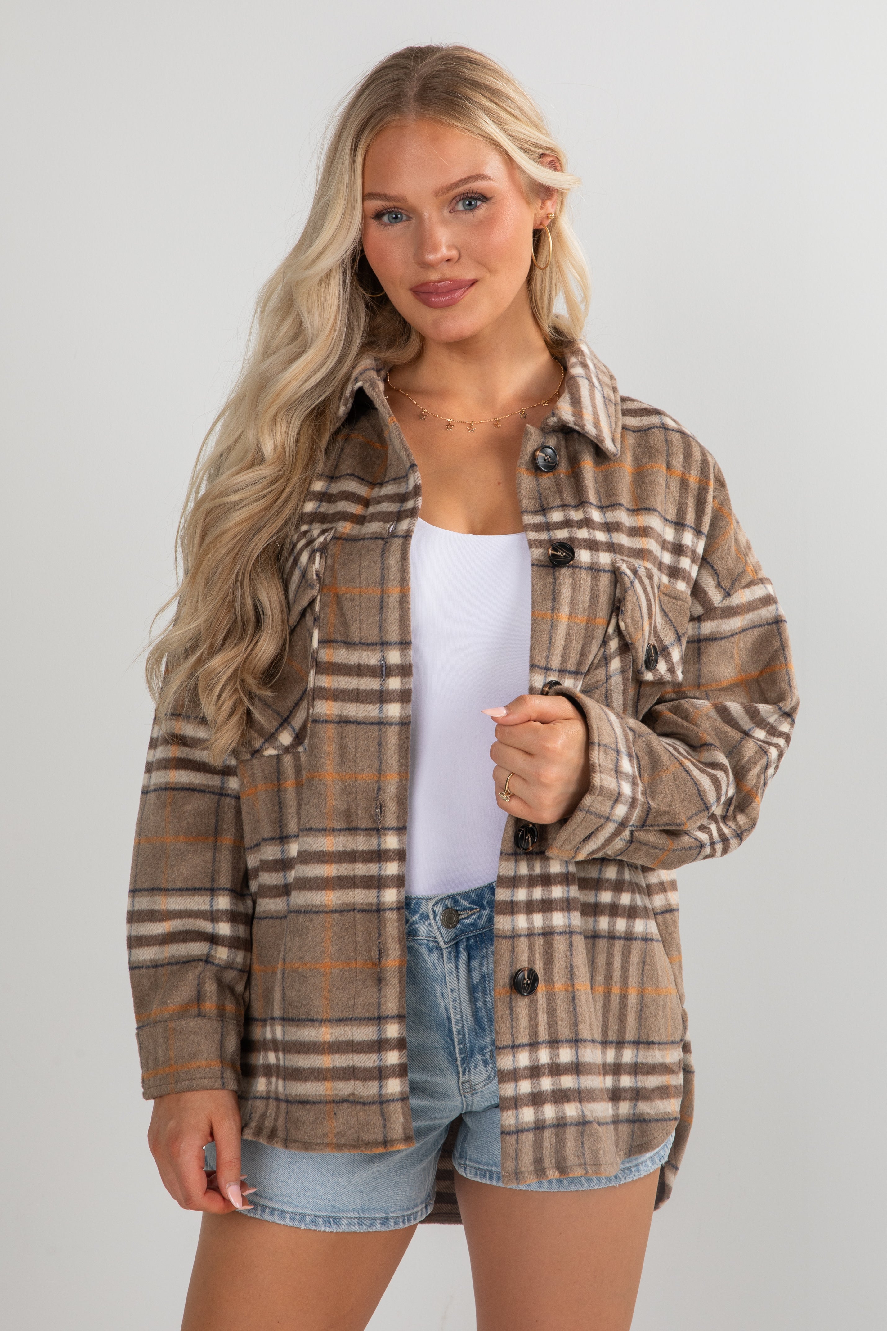 Woman wearing a plaid shirt over a white top and denim shorts on a plain background