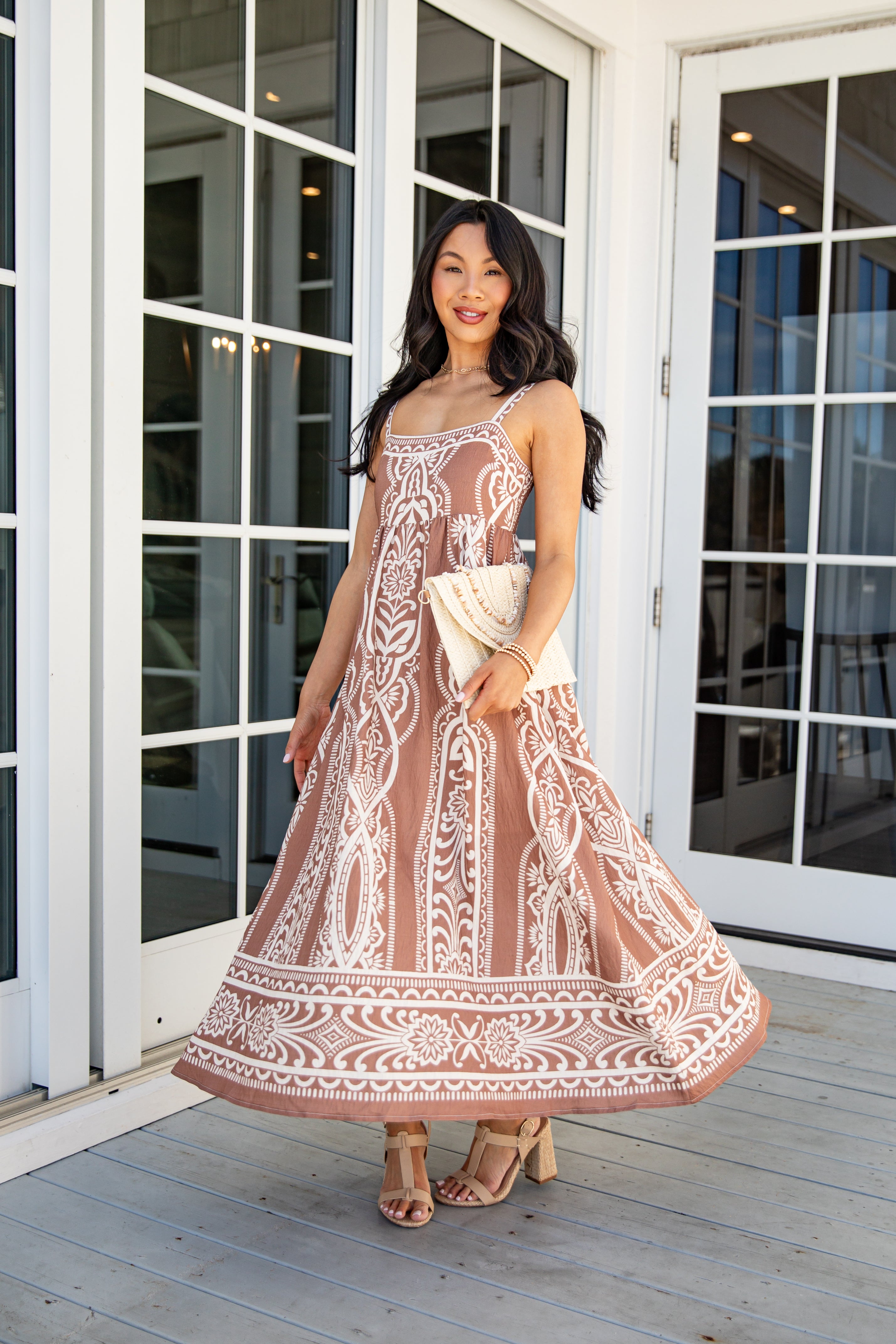 Woman in a patterned dress standing on a wooden deck with glass doors in the background