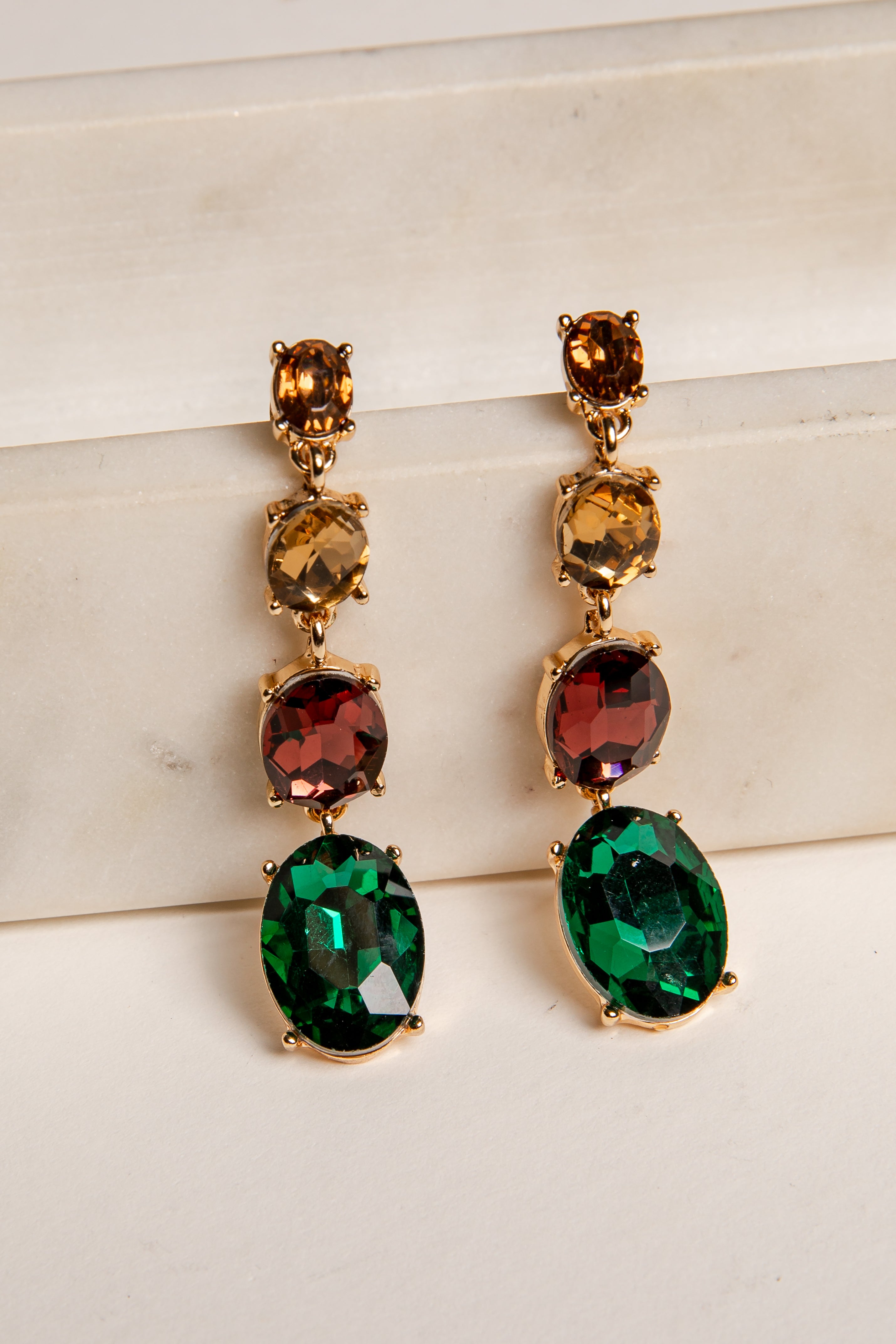 Pair of gold earrings with green and red gemstones on a light background