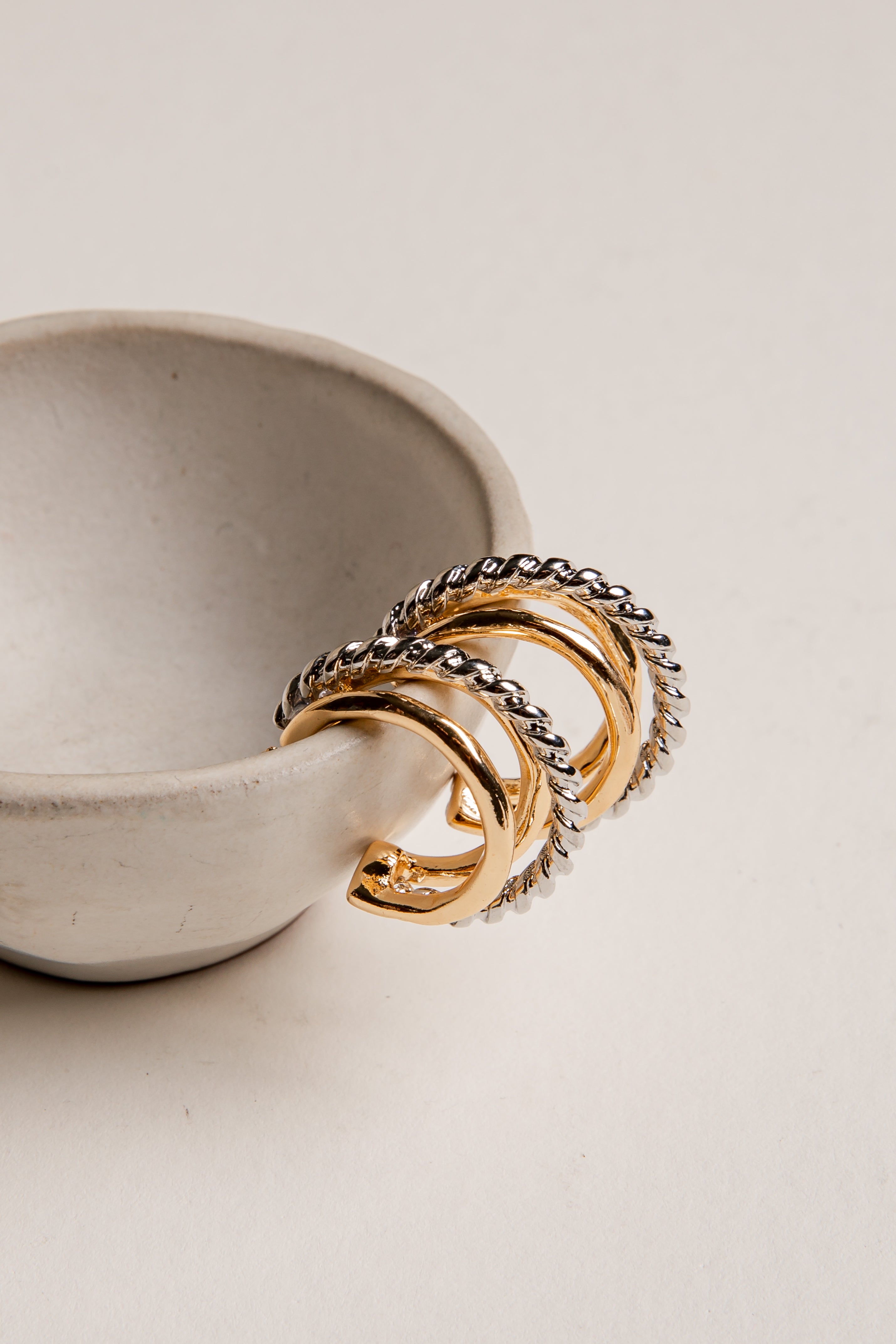 Three gold rings with braided designs on a white ceramic dish.