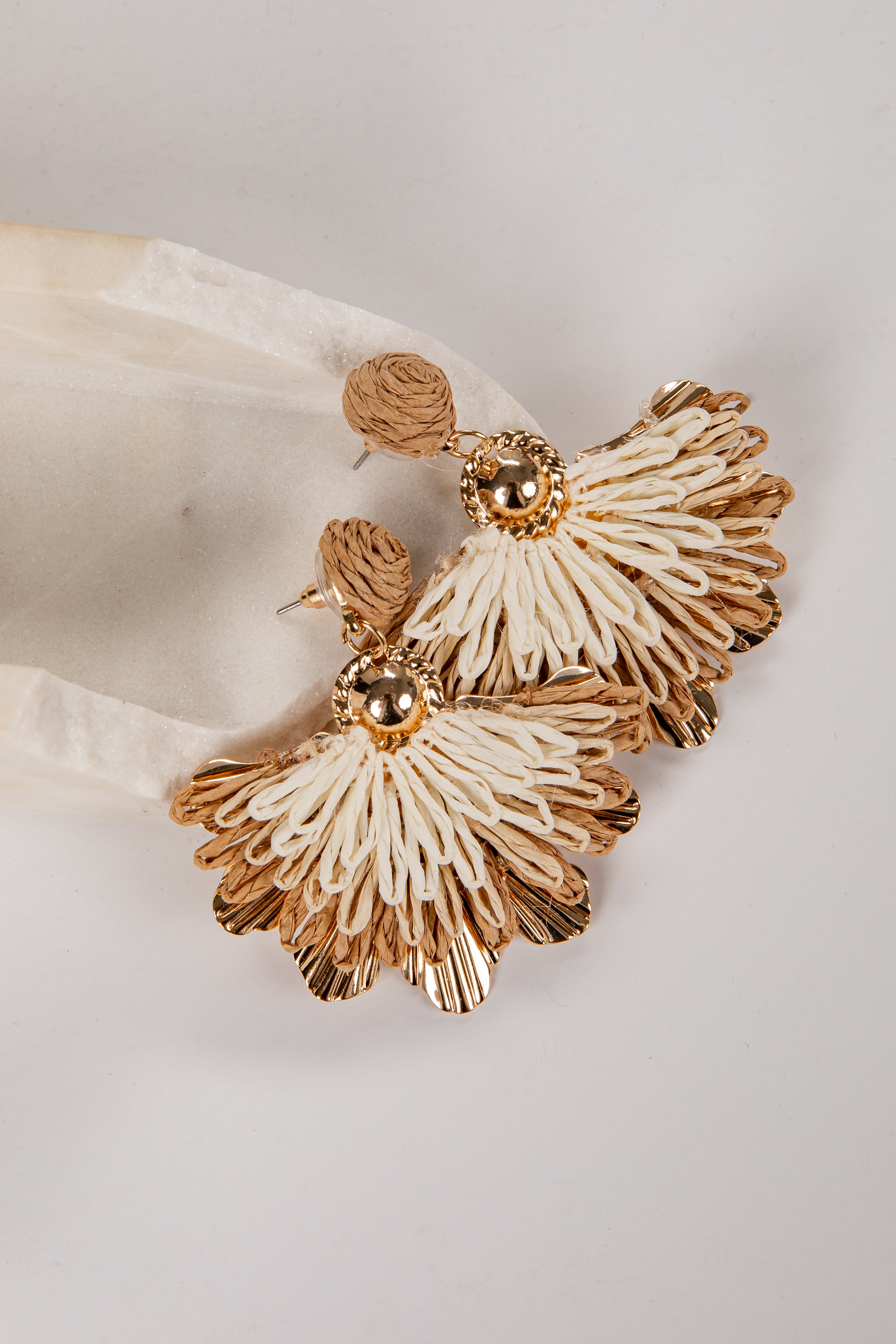 Pair of gold and white earrings on a light fabric background