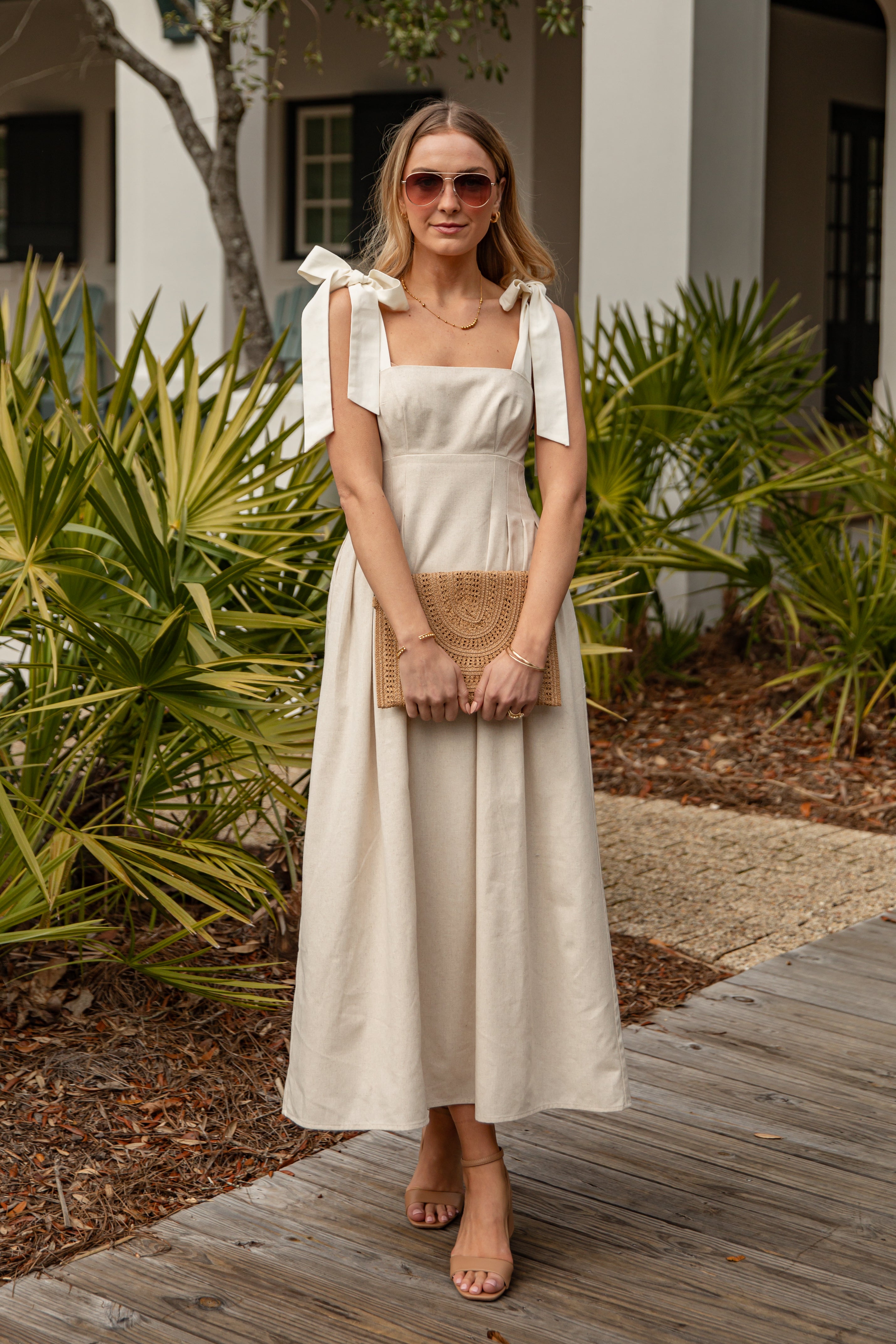 Woman in a white dress standing outdoors with plants and a building in the background