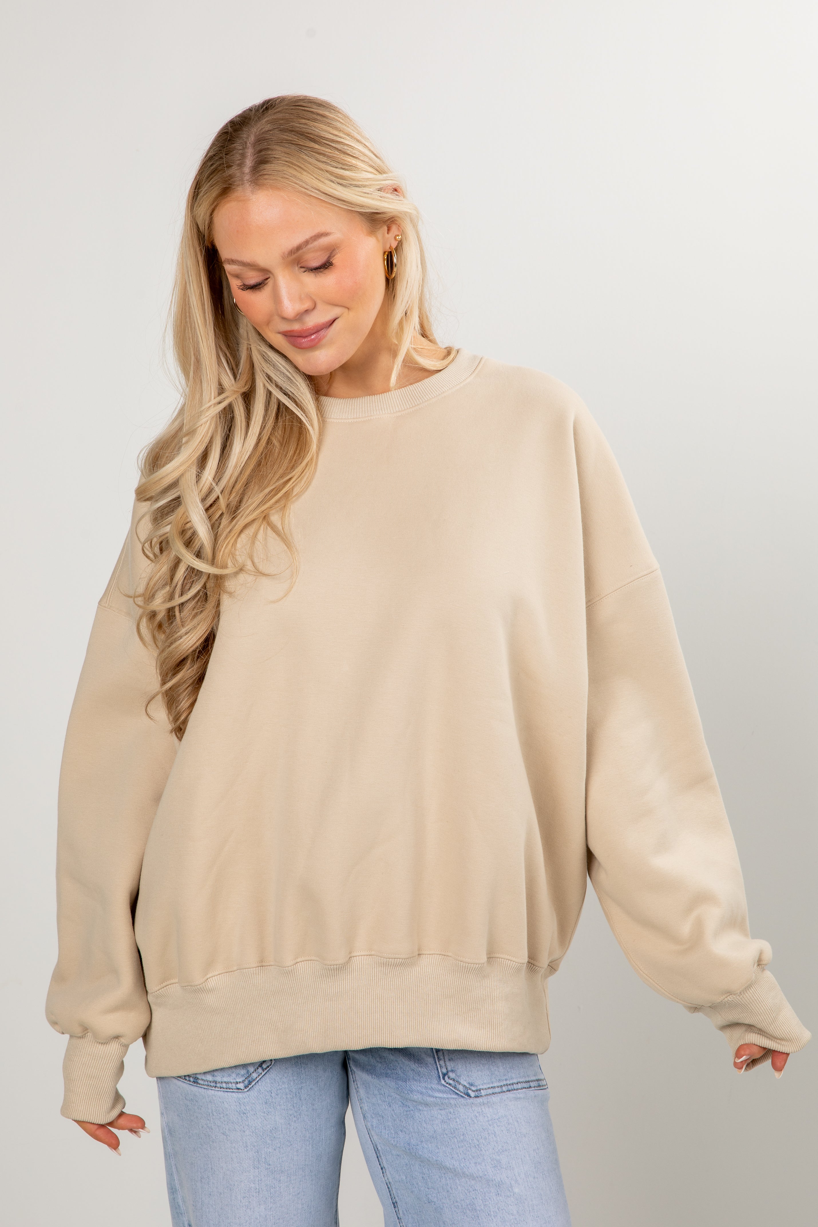 Woman wearing a beige sweater and light blue jeans against a plain background