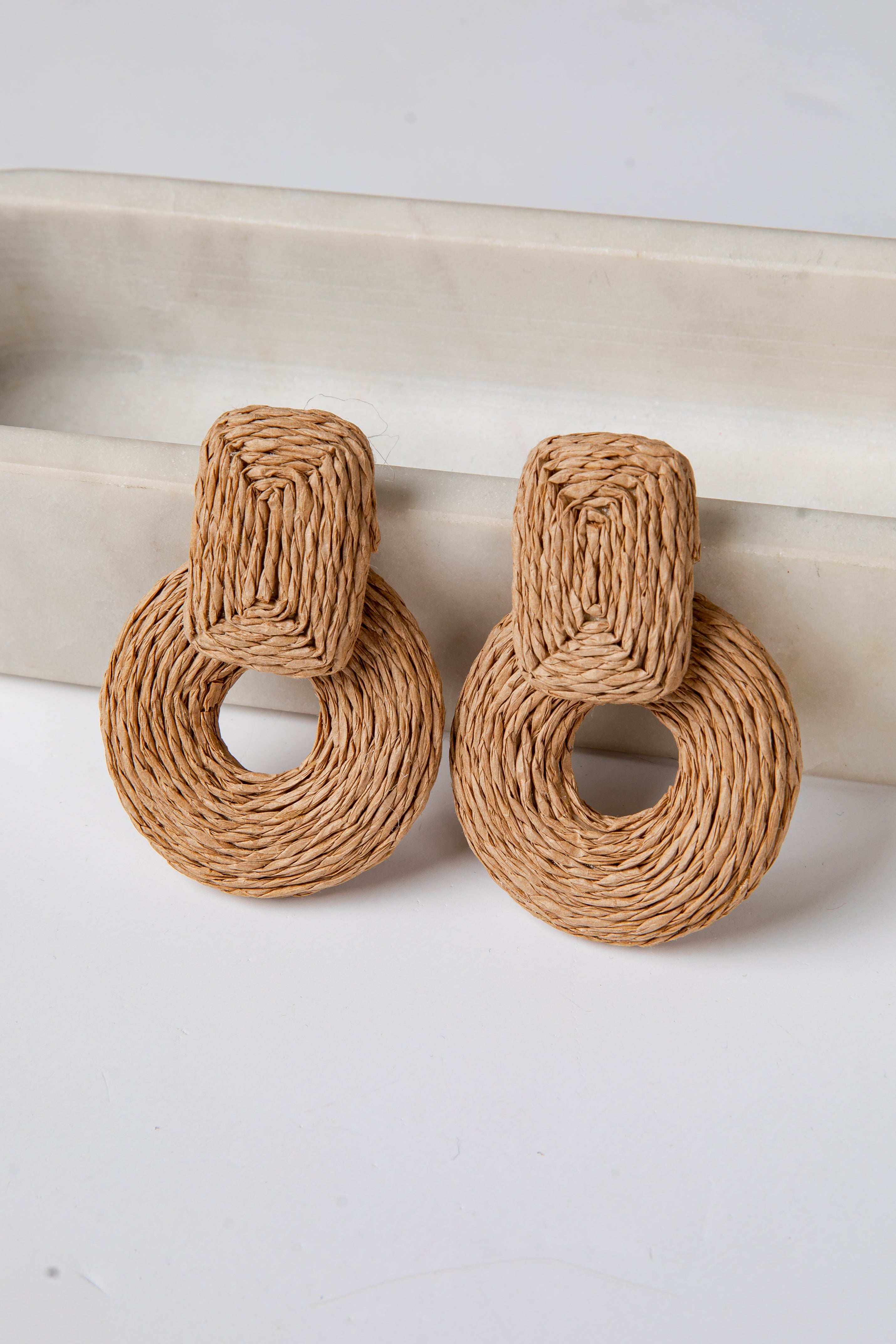 Pair of woven brown earrings on a white surface with a neutral background