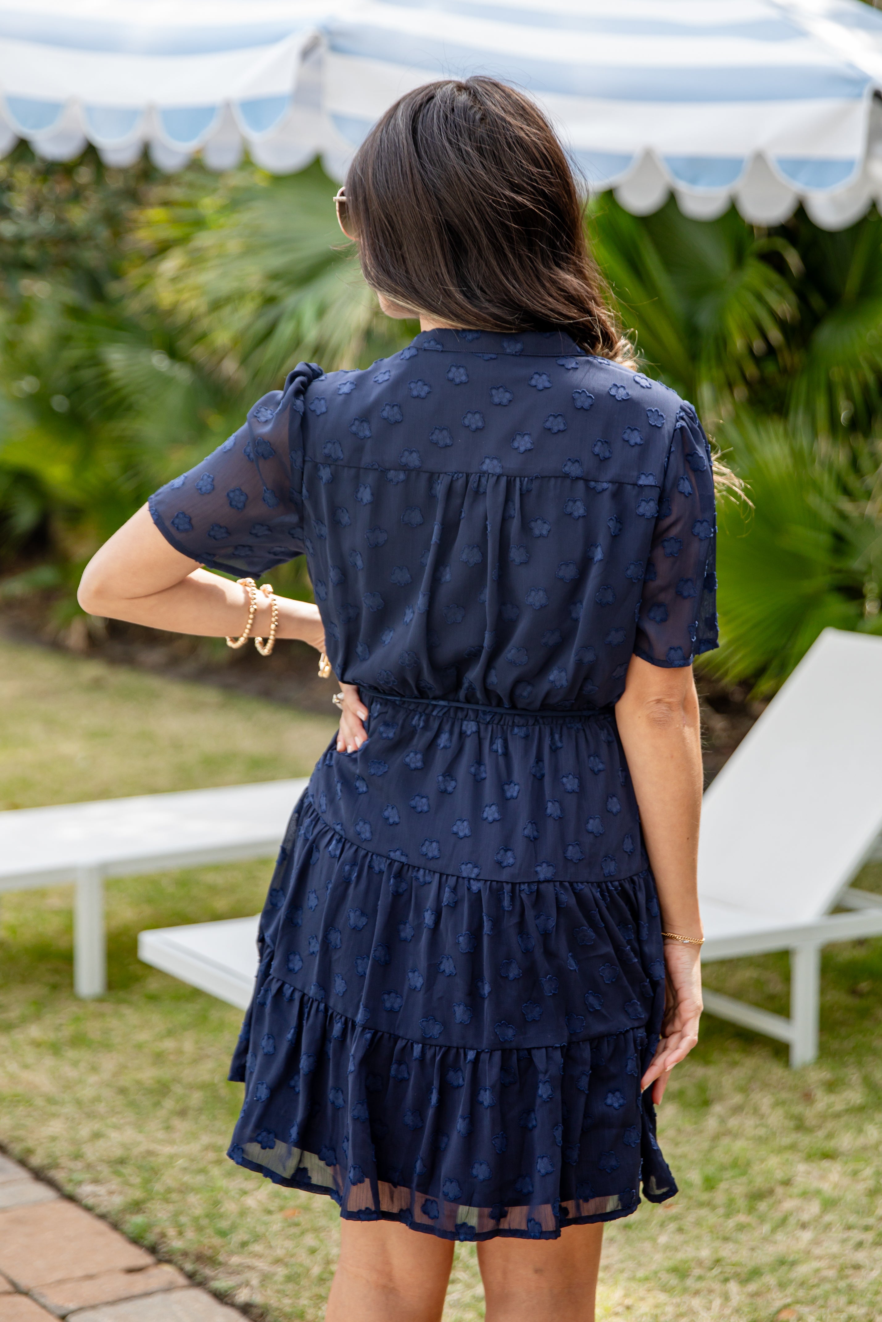 Woman in a navy blue dress standing outdoors with lounge chairs and greenery in the background