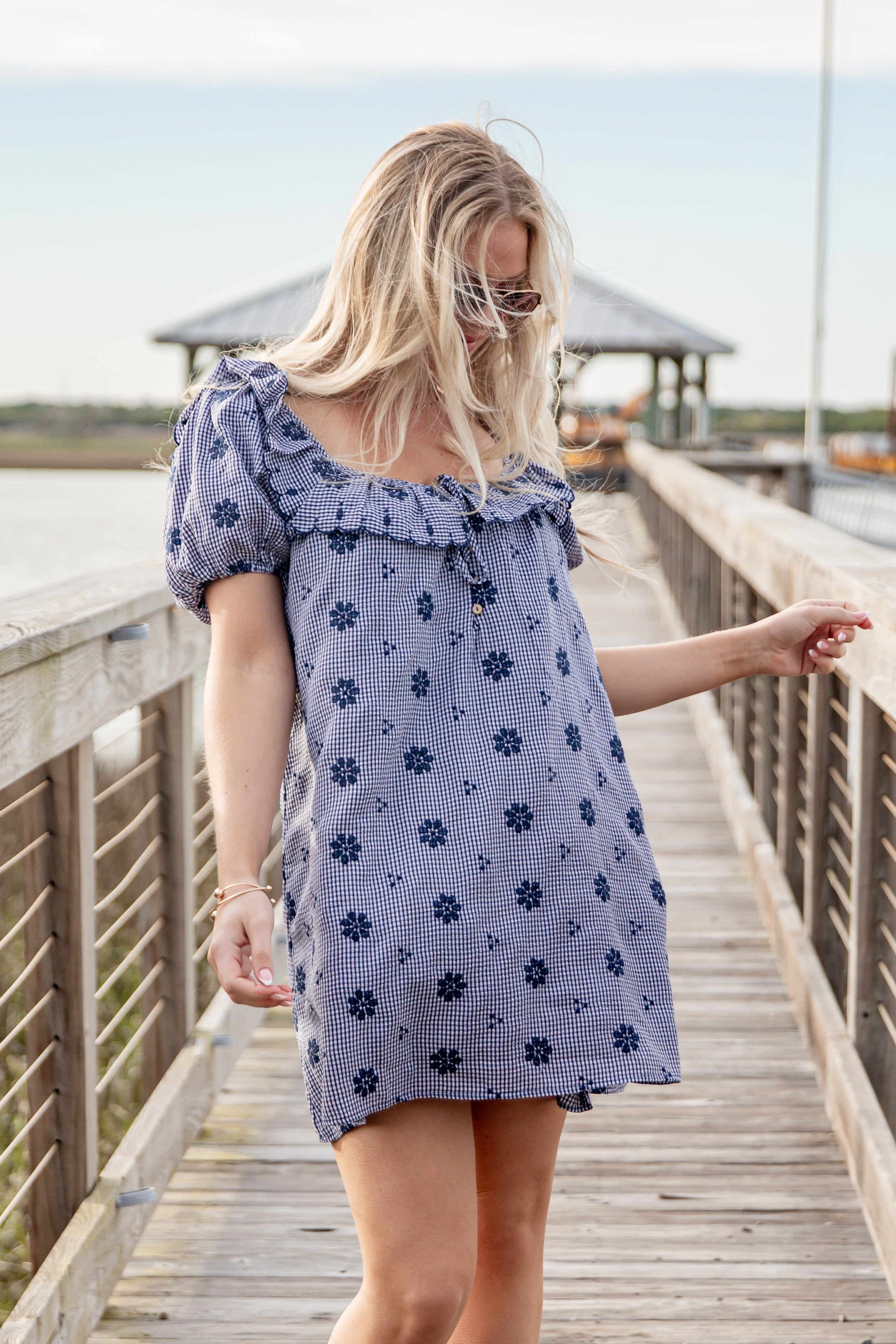 Woman in a blue floral dress standing on a wooden boardwalk.