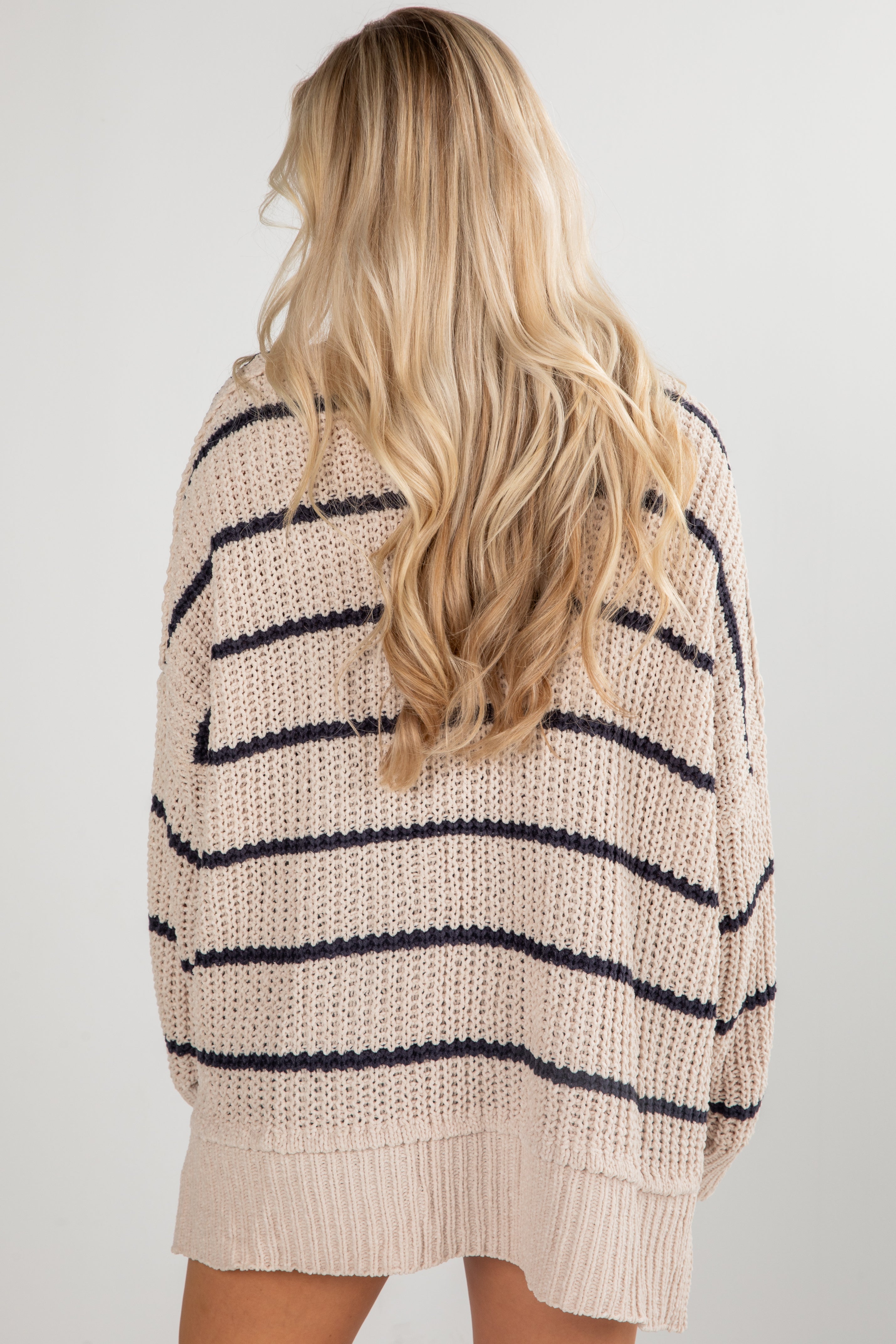 Person wearing a beige and navy striped sweater on a plain background