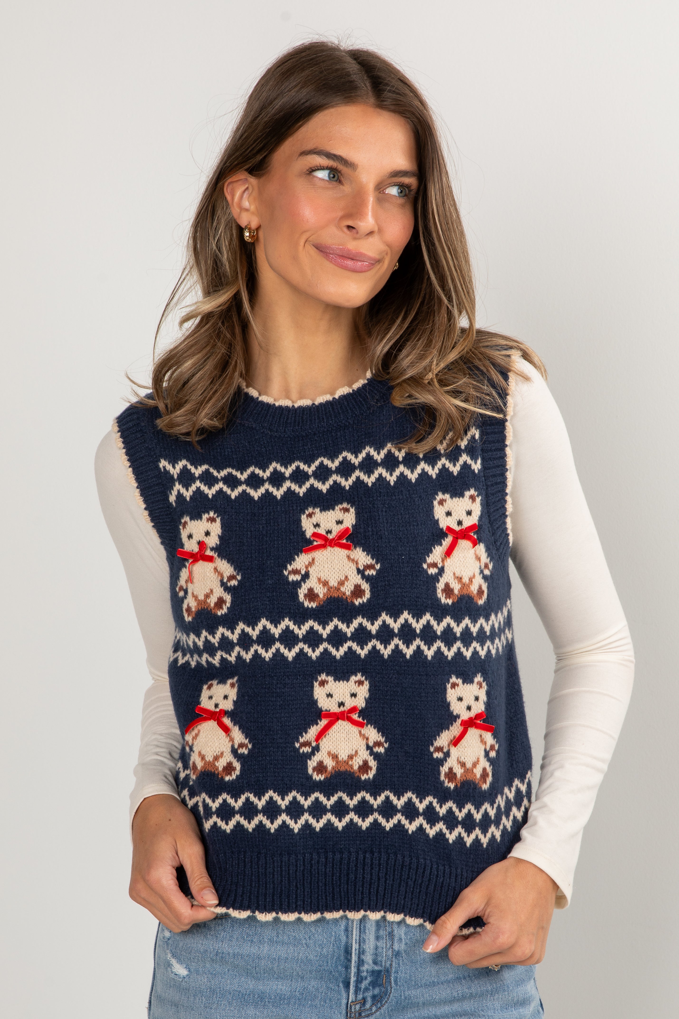 Woman wearing a navy blue sweater vest with teddy bear patterns on a light gray background