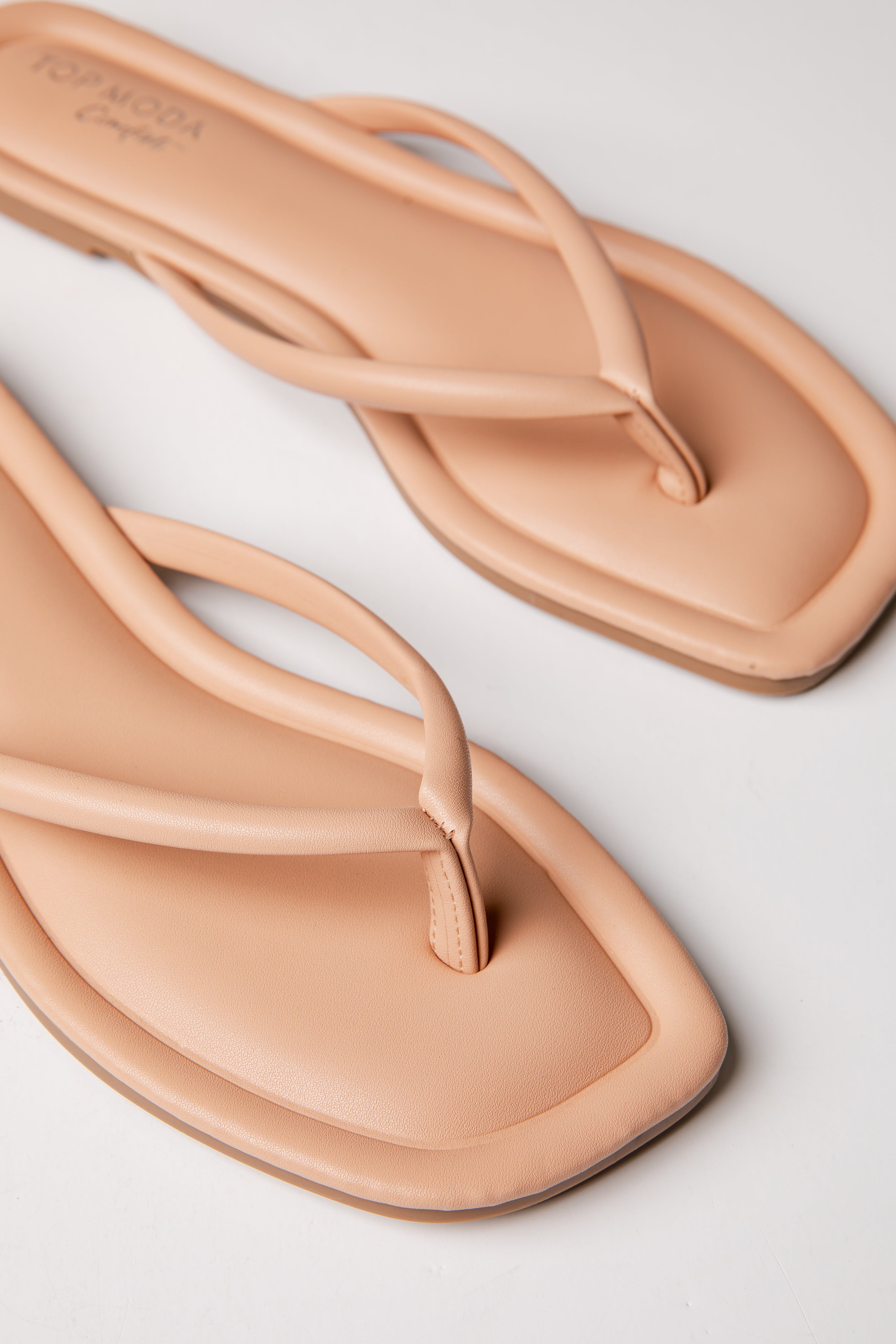 Pair of beige flip-flops on a light gray background