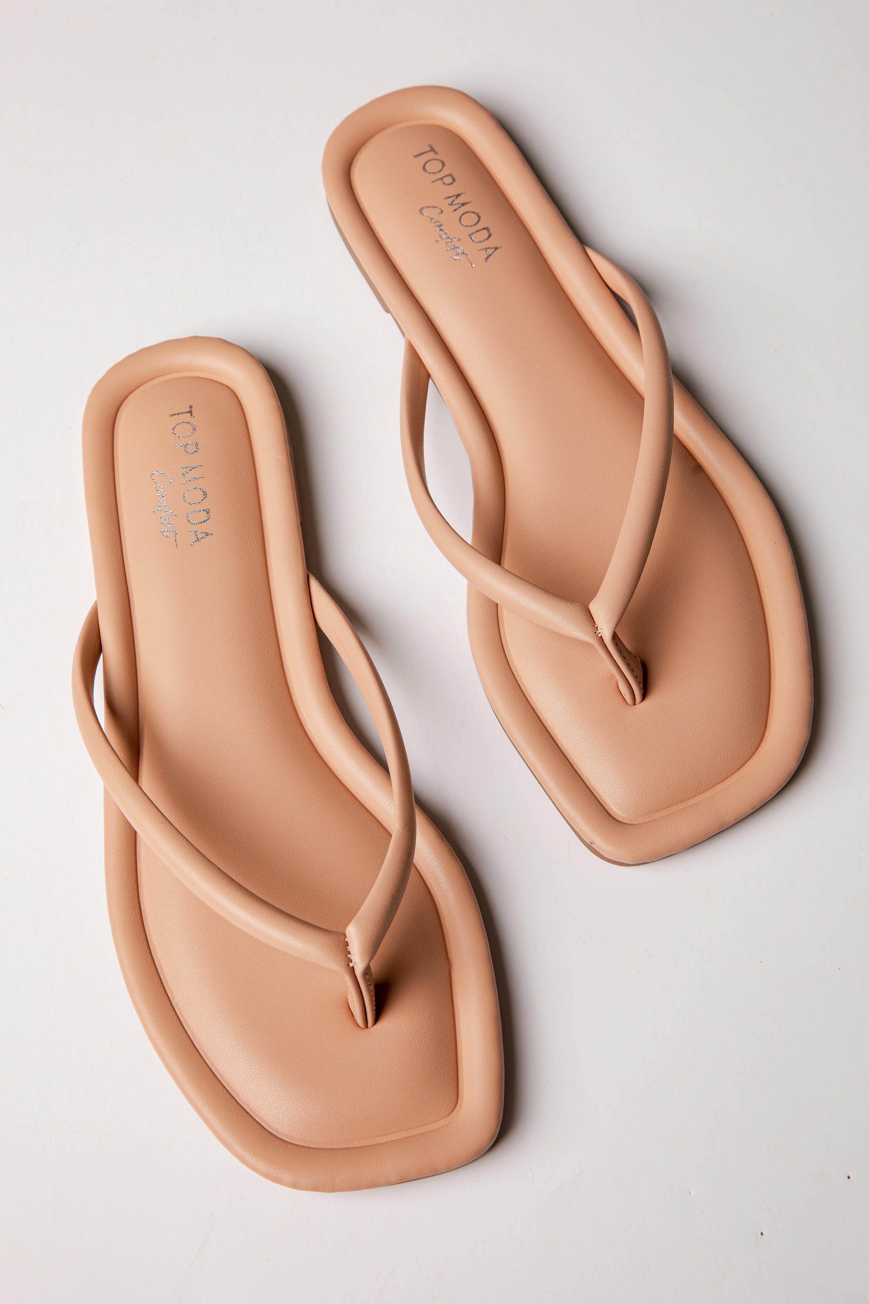 Pair of tan flip-flops on a light gray background