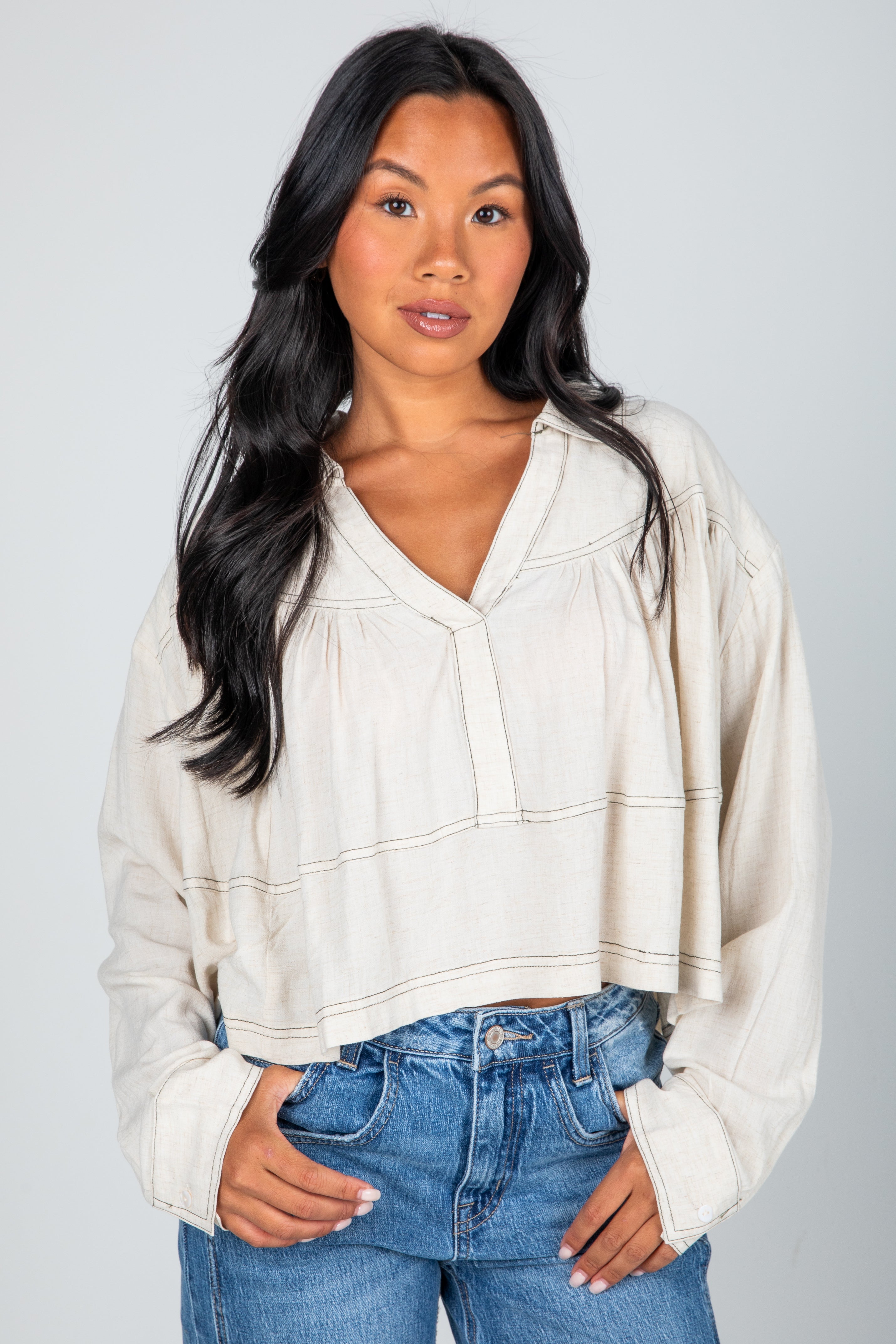 Woman wearing a beige blouse and blue jeans against a gray background