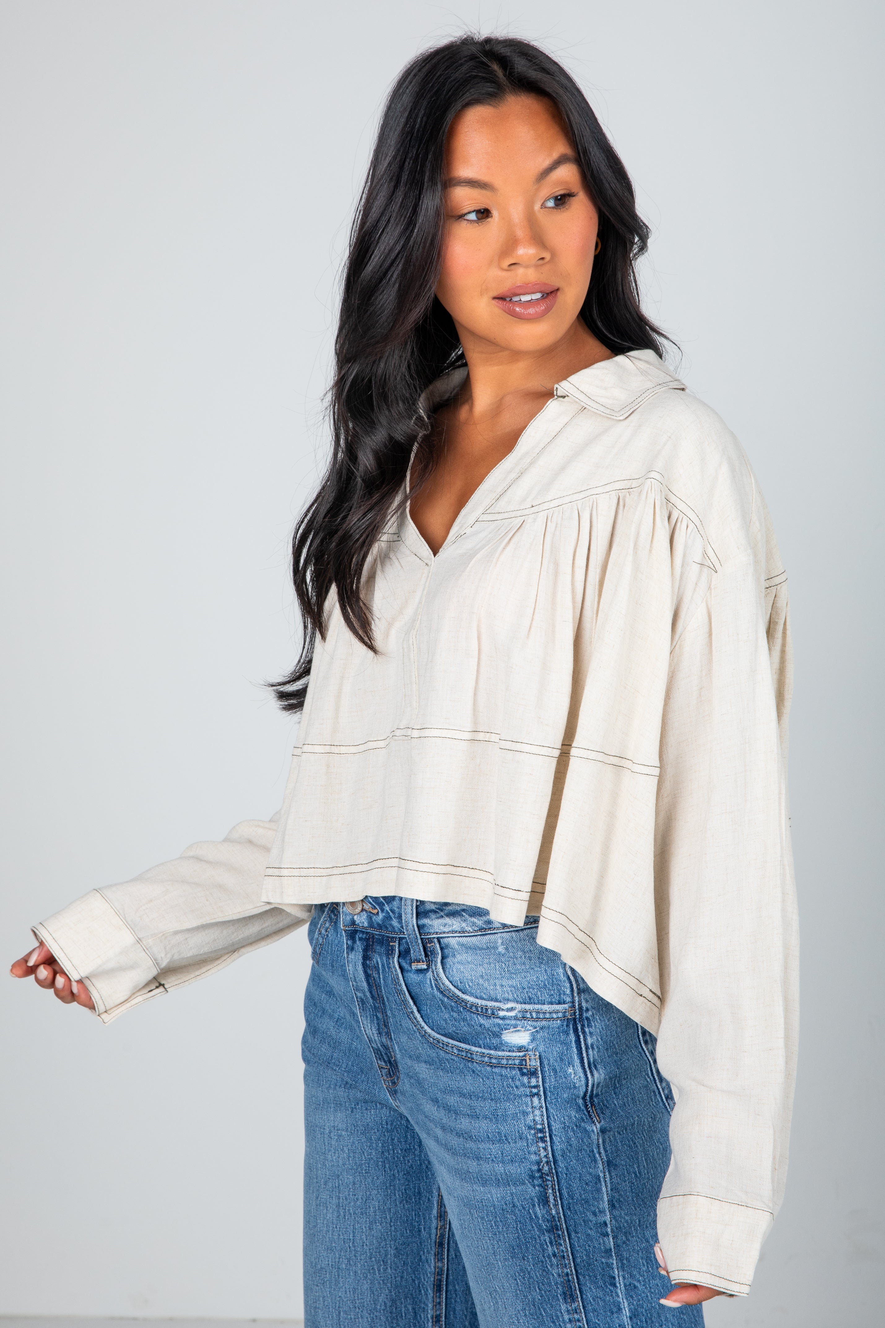 Woman wearing a cream-colored hoodie and blue jeans against a gray background