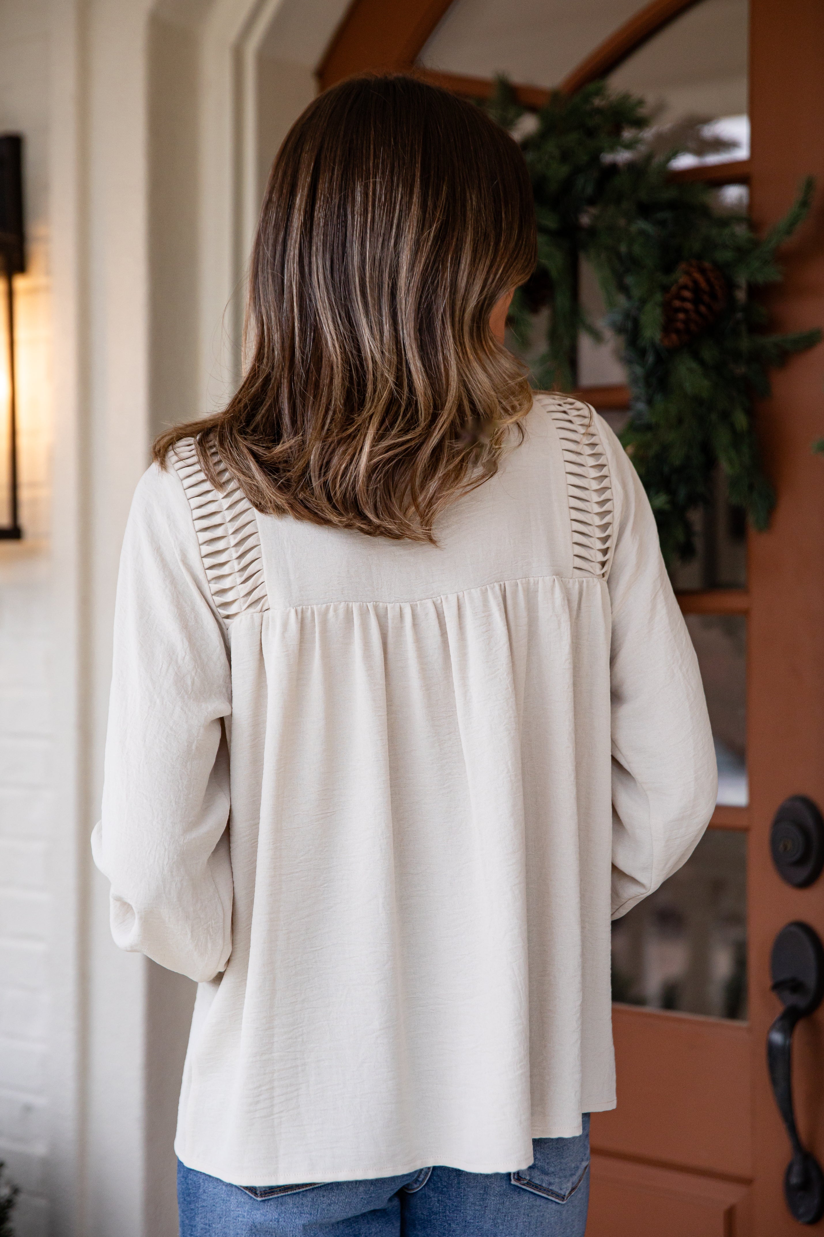 Woman wearing a beige blouse with lace details in front of a door with a wreath.