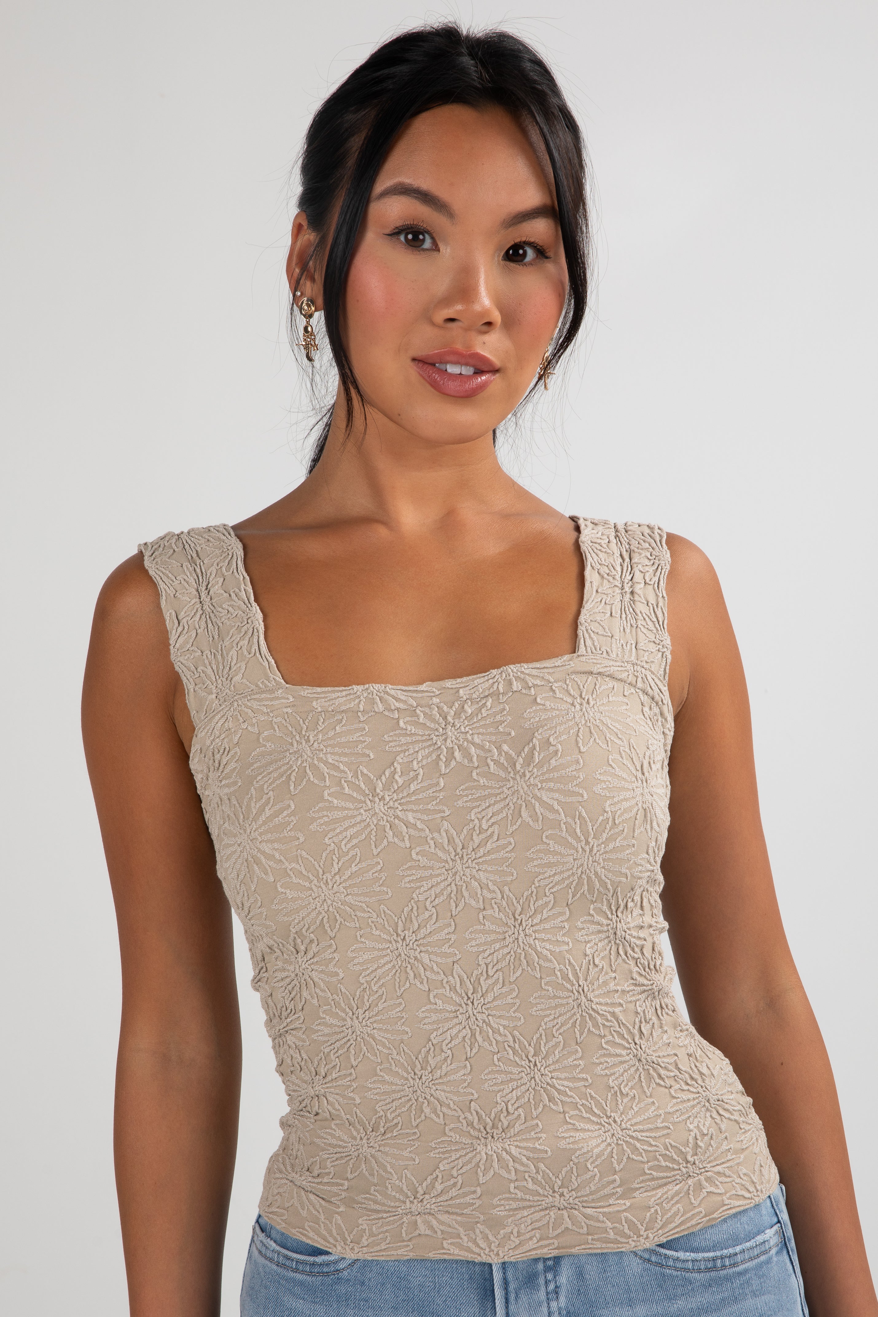 Woman wearing a beige sleeveless top with floral patterns on a plain background
