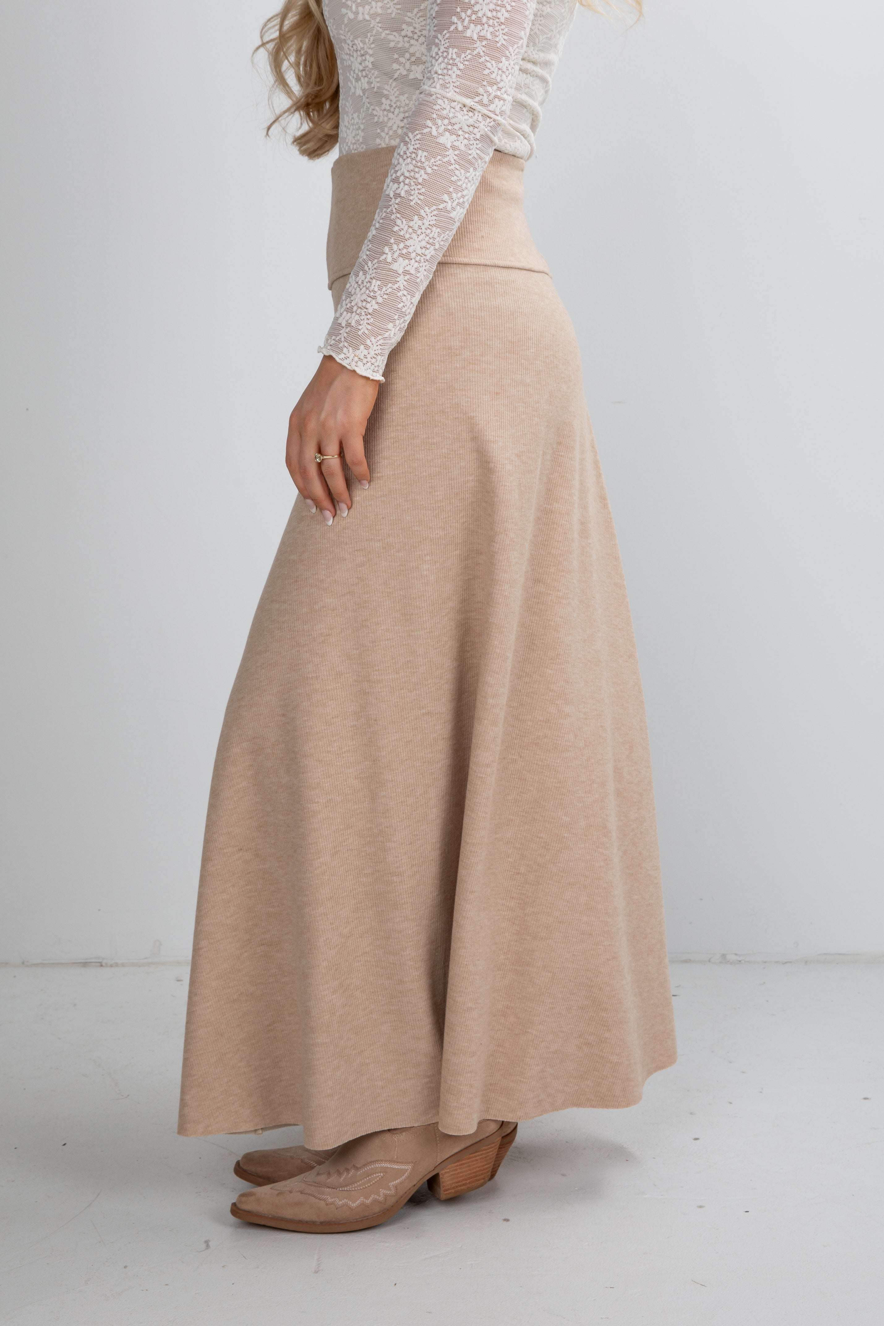 Person wearing a beige skirt and white lace top on a plain background