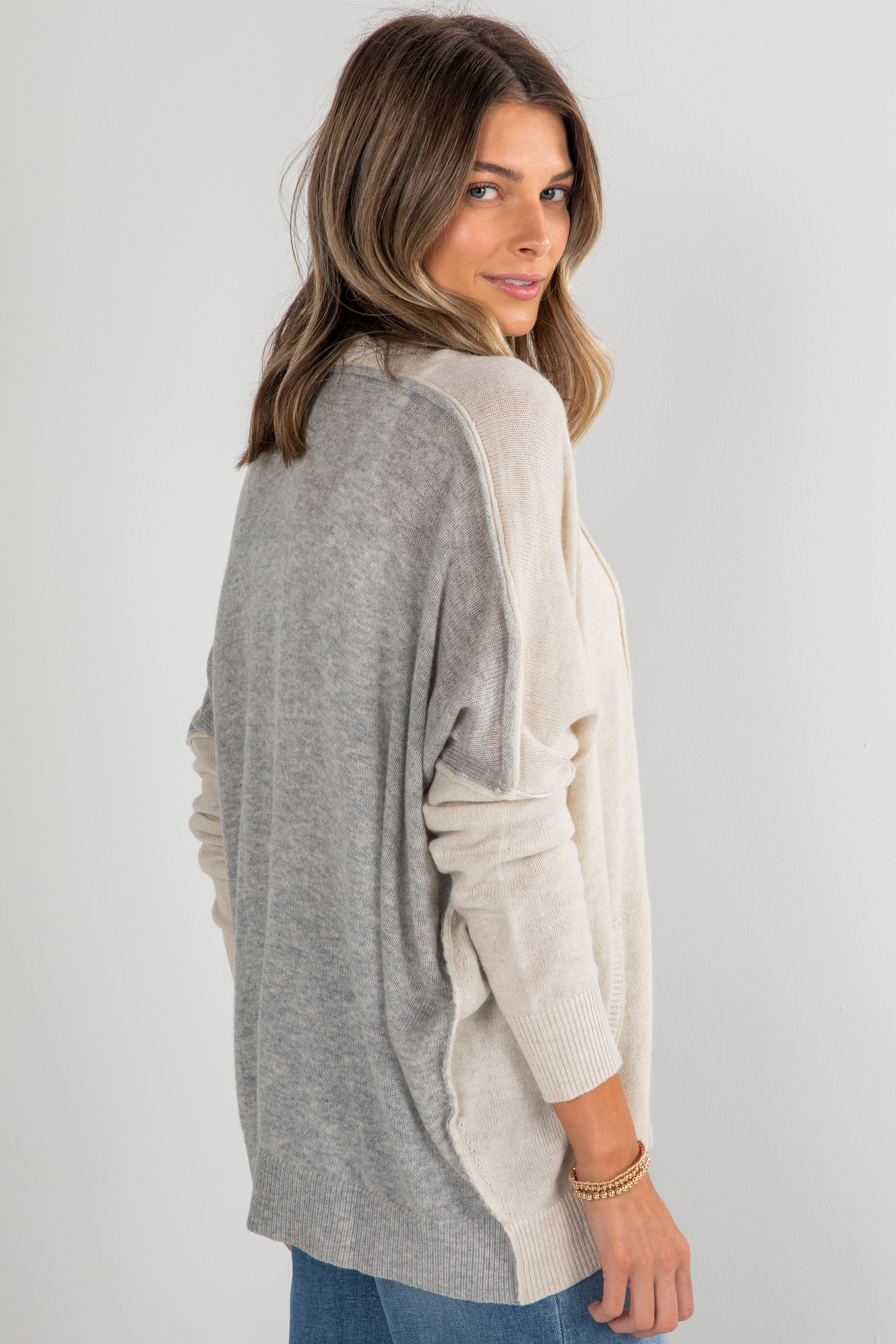 Woman wearing a gray and beige color-blocked sweater on a plain background