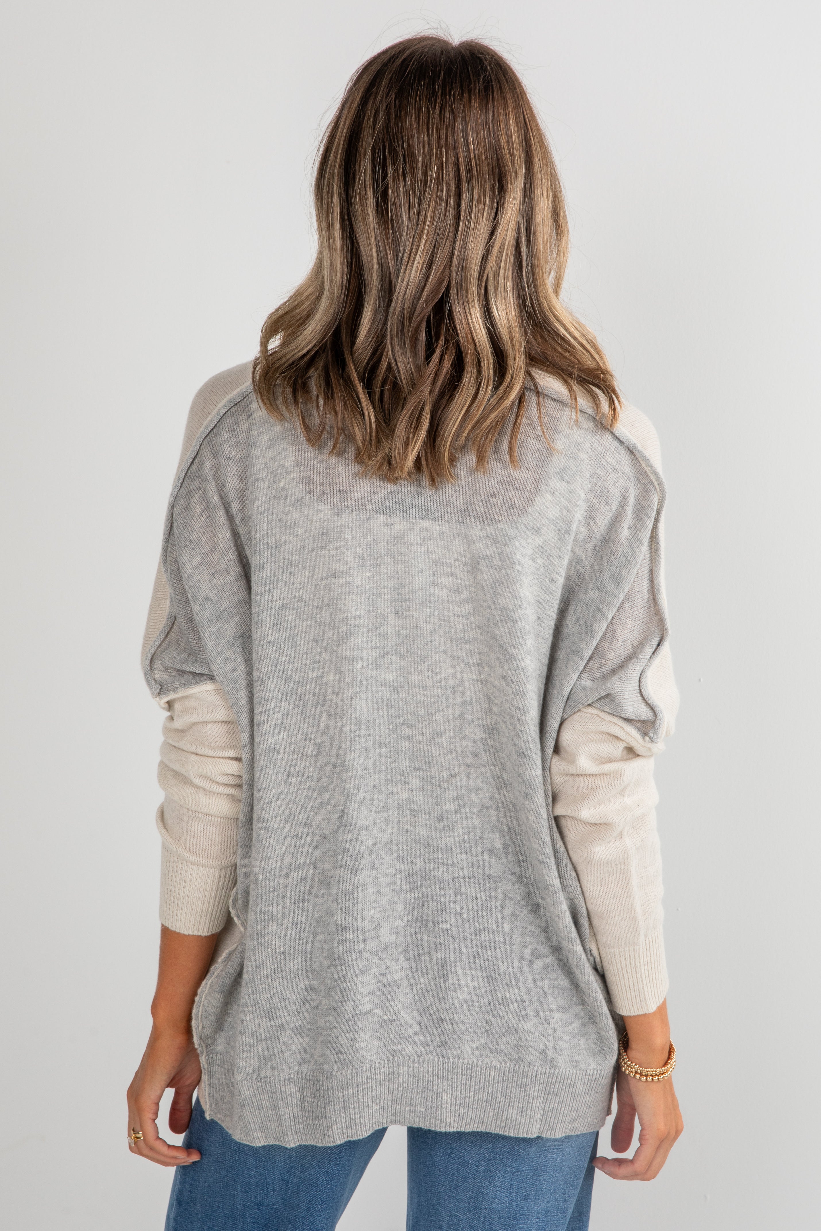 Woman wearing a gray and beige long-sleeve top with a plain background