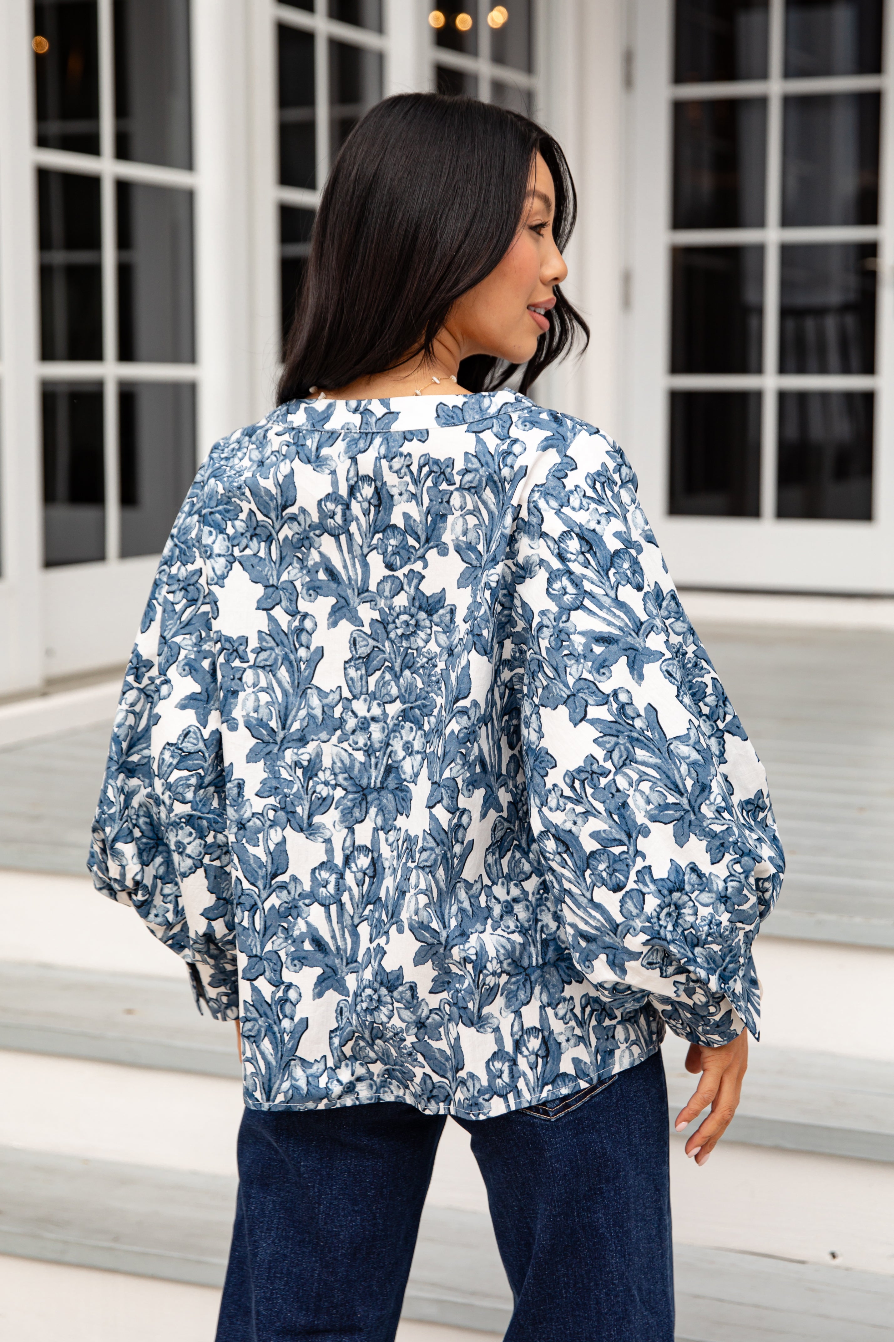 Woman wearing a blue and white floral jacket standing on steps.