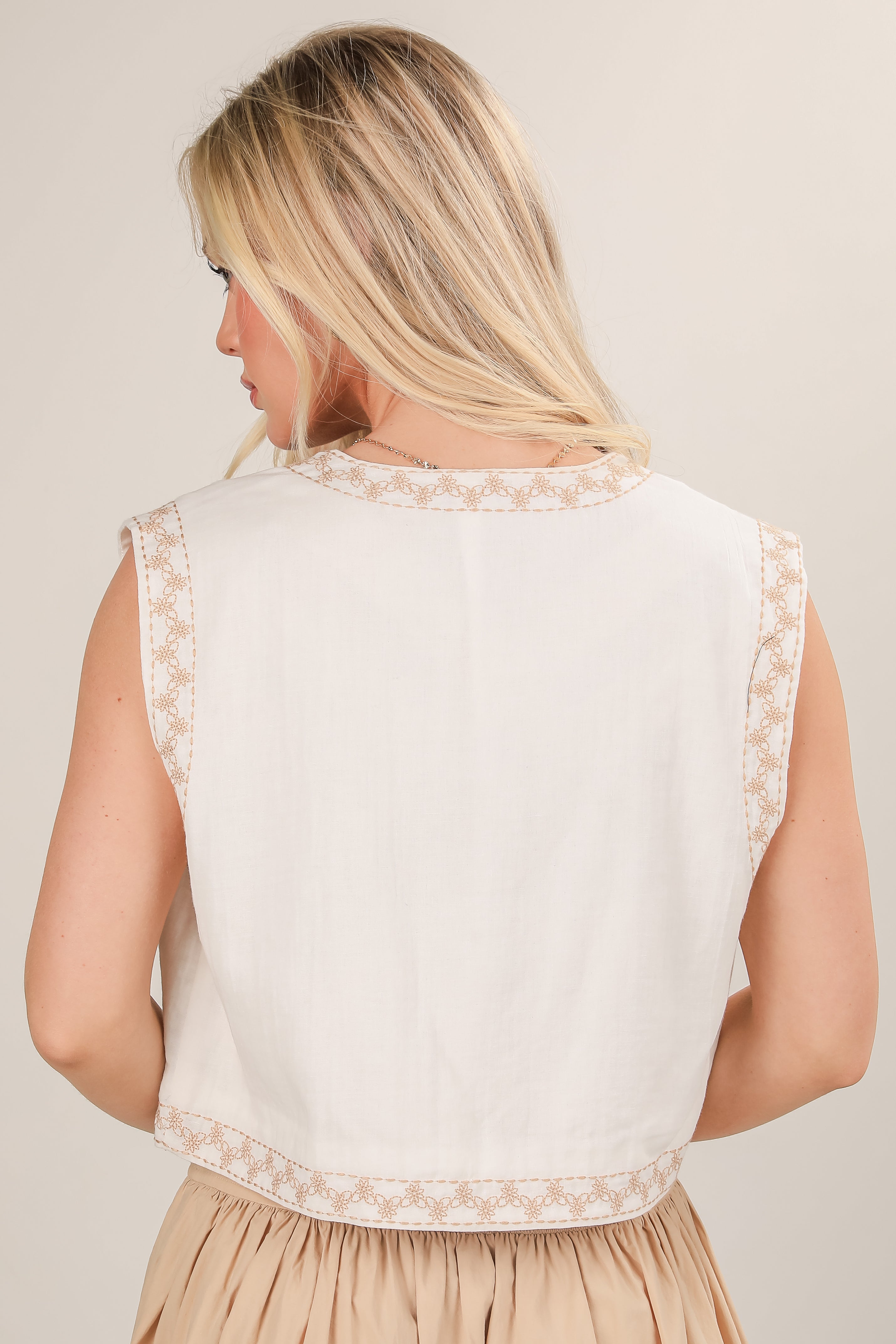 Woman wearing a white sleeveless top with lace details on a beige background