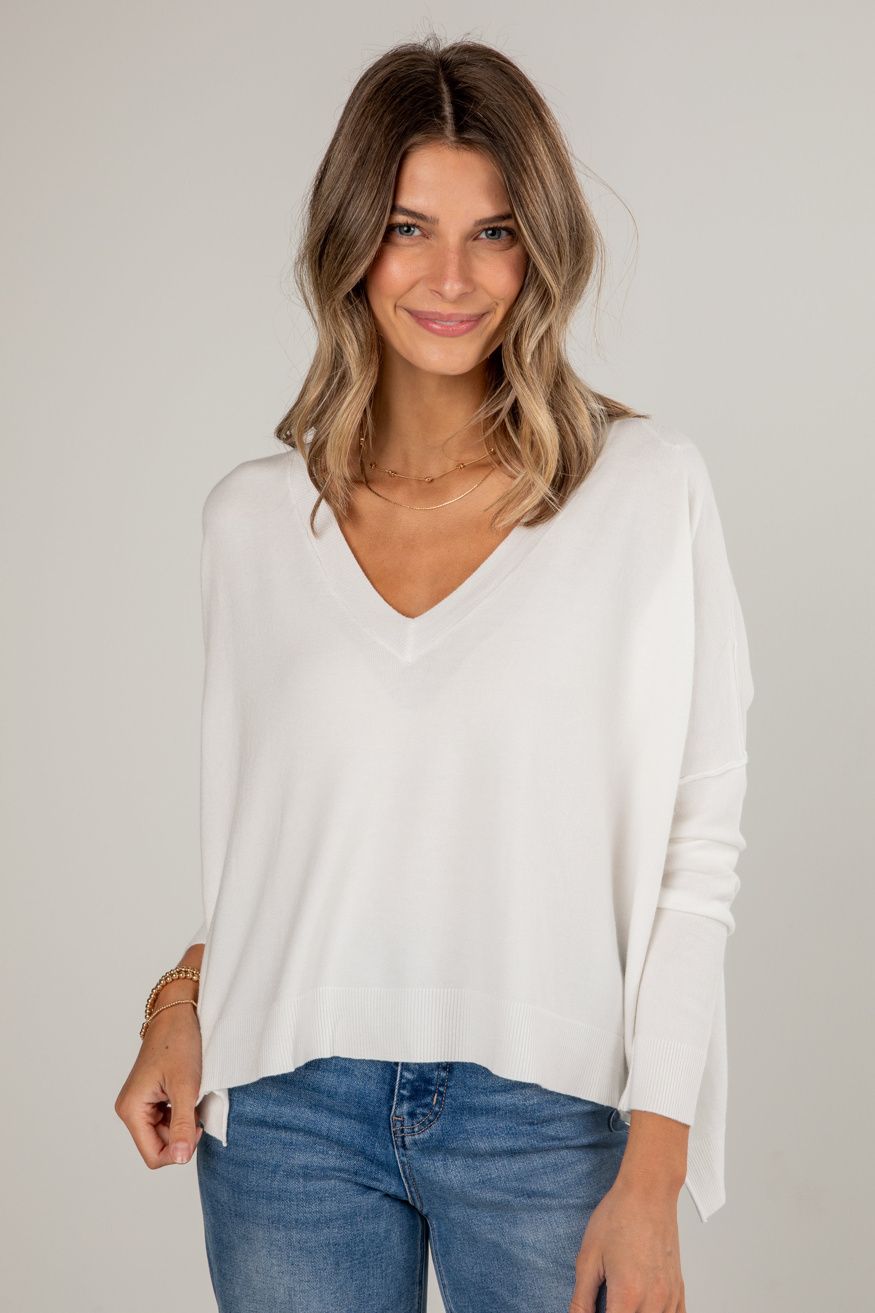 Woman wearing a white sweater and blue jeans against a plain background
