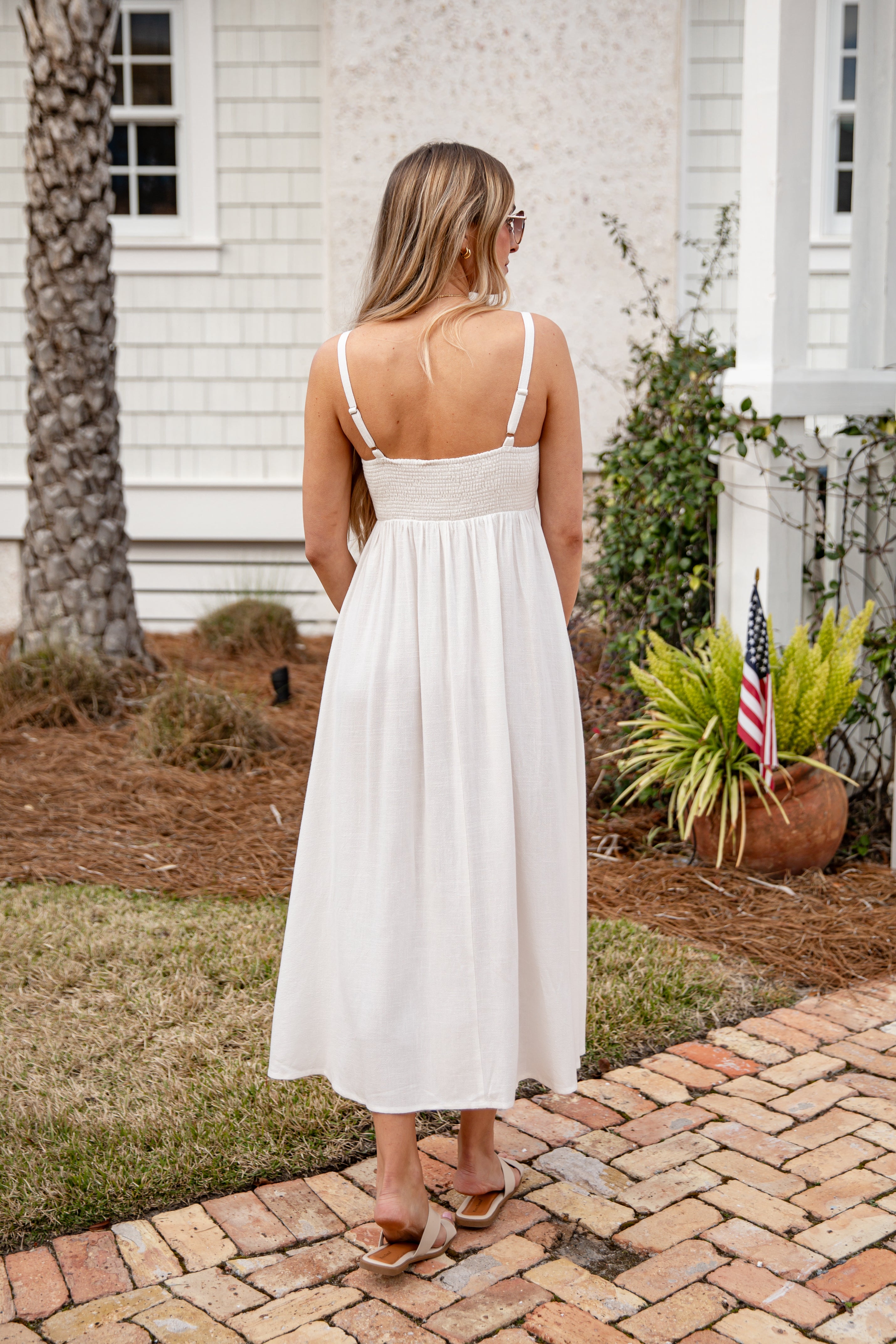 Woman in a white dress standing on a brick path in front of a house.