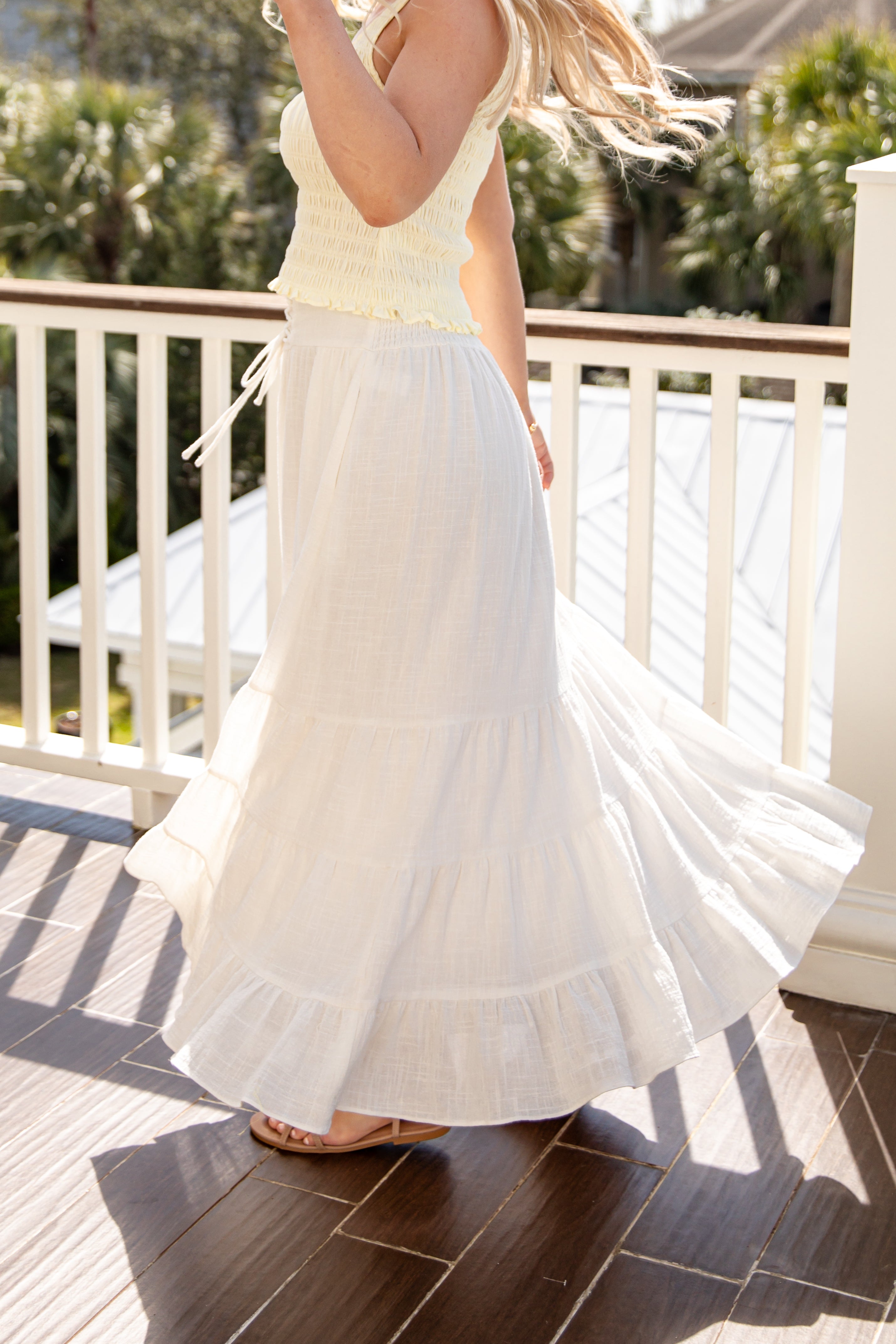 Woman wearing a white dress on a wooden deck with greenery in the background