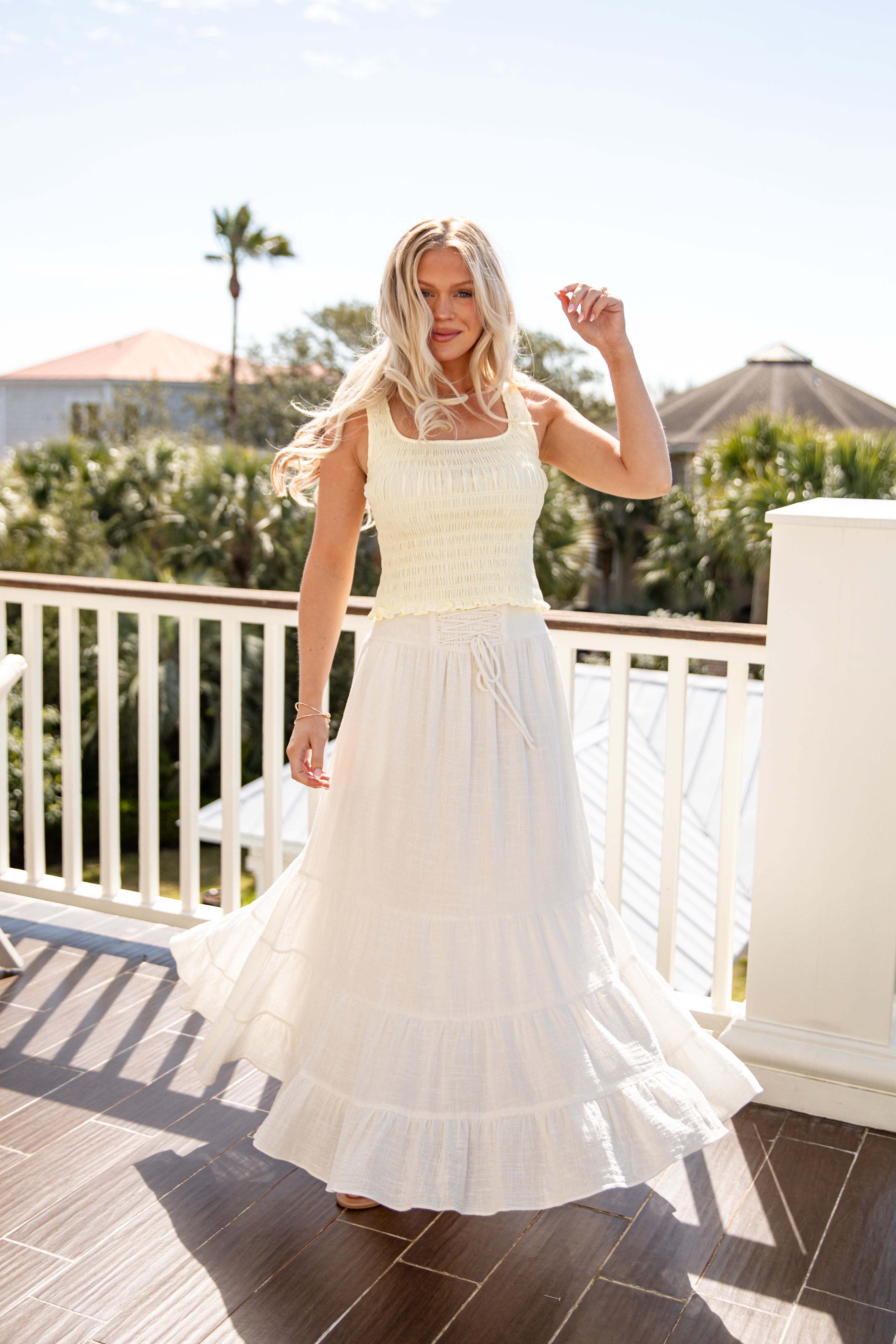 Woman in a white dress standing on a balcony with trees and buildings in the background