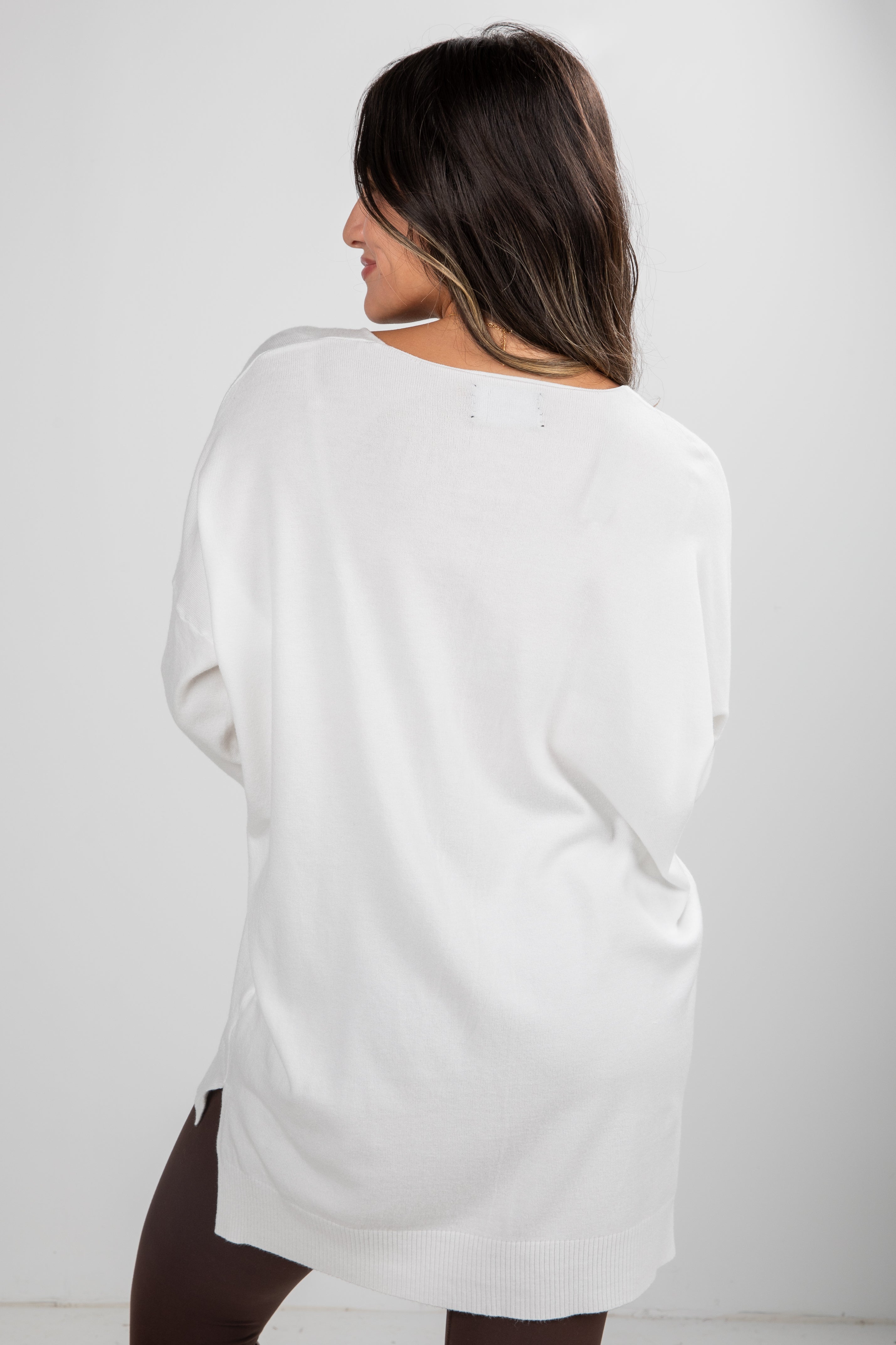 Woman wearing a white oversized sweater against a plain background