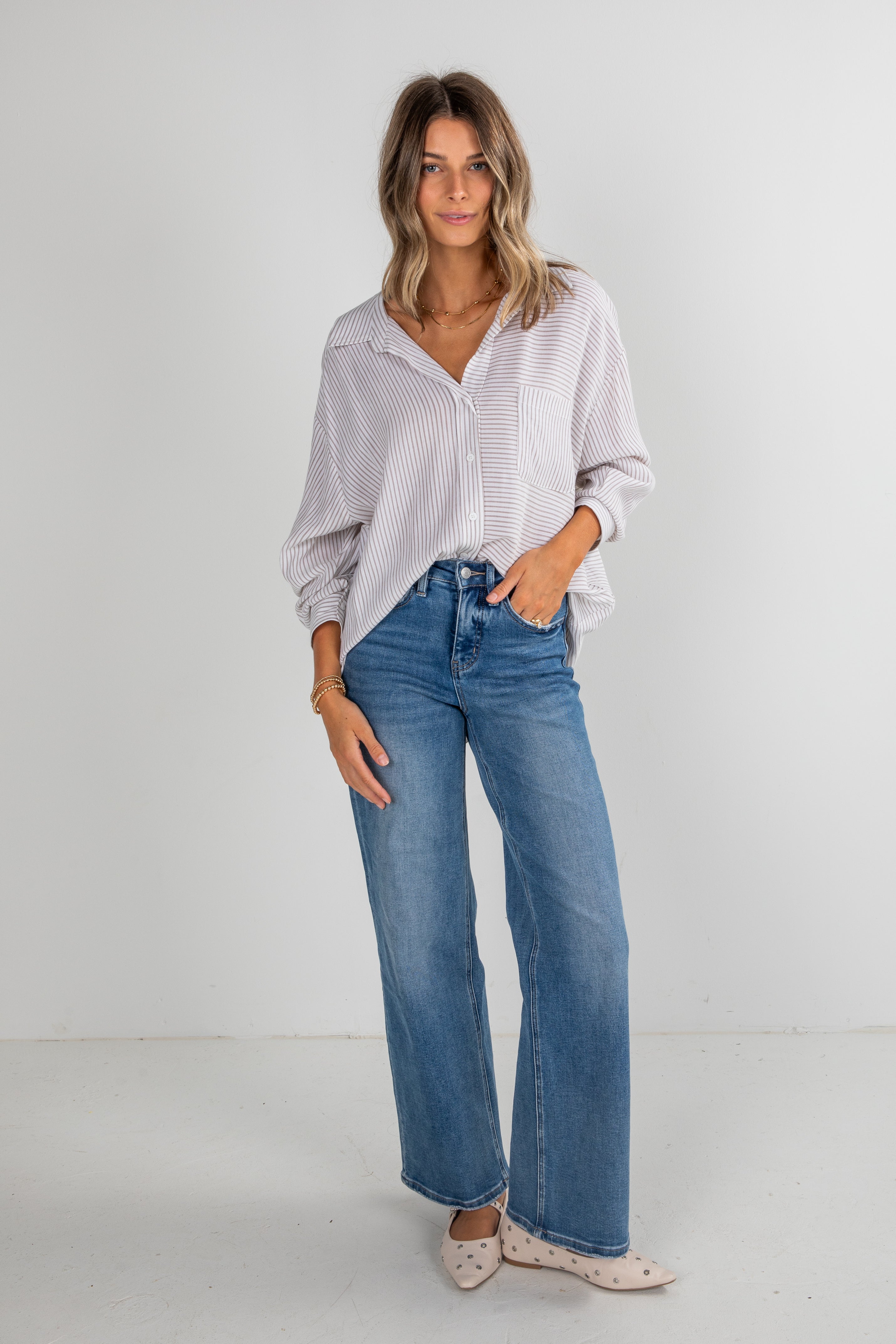 Woman wearing a white patterned shirt and blue jeans on a plain background